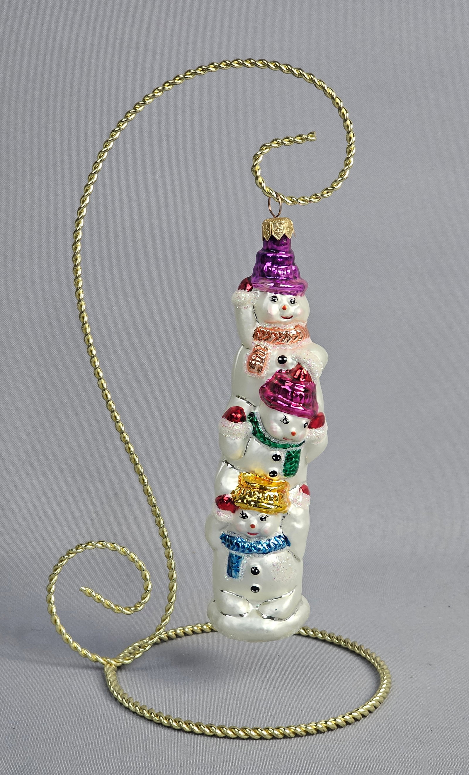 Christopher Radko Glass Stacked Snowmen Ornament: Stand not included. This mouth-blown glass Christmas ornament is a design by Christopher Radko featuring a vertical stack of three festive snowmen. The ornament is hand-painted with metallic and lacqu