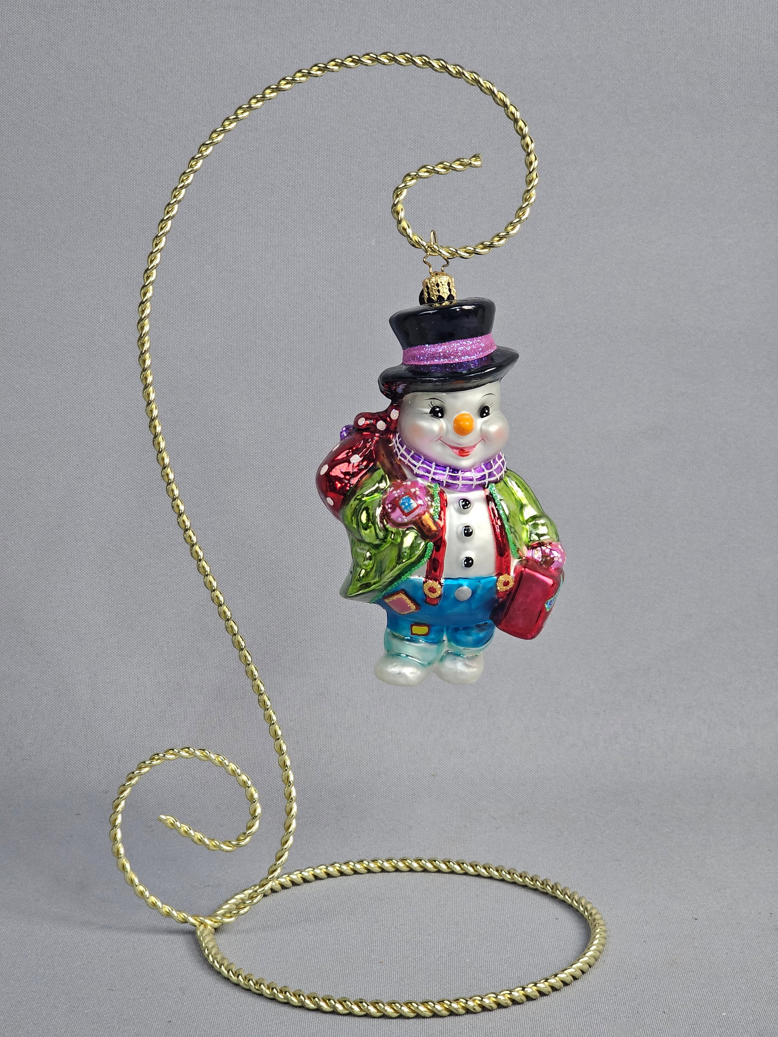 Christopher Radko Glass Traveling Snowman Ornament: Stand not included. A hand-blown glass Christmas ornament by Christopher Radko, identified as the Snowy Travels or World Traveler Snowman design. The ornament depicts a whimsical snowman figure wearin