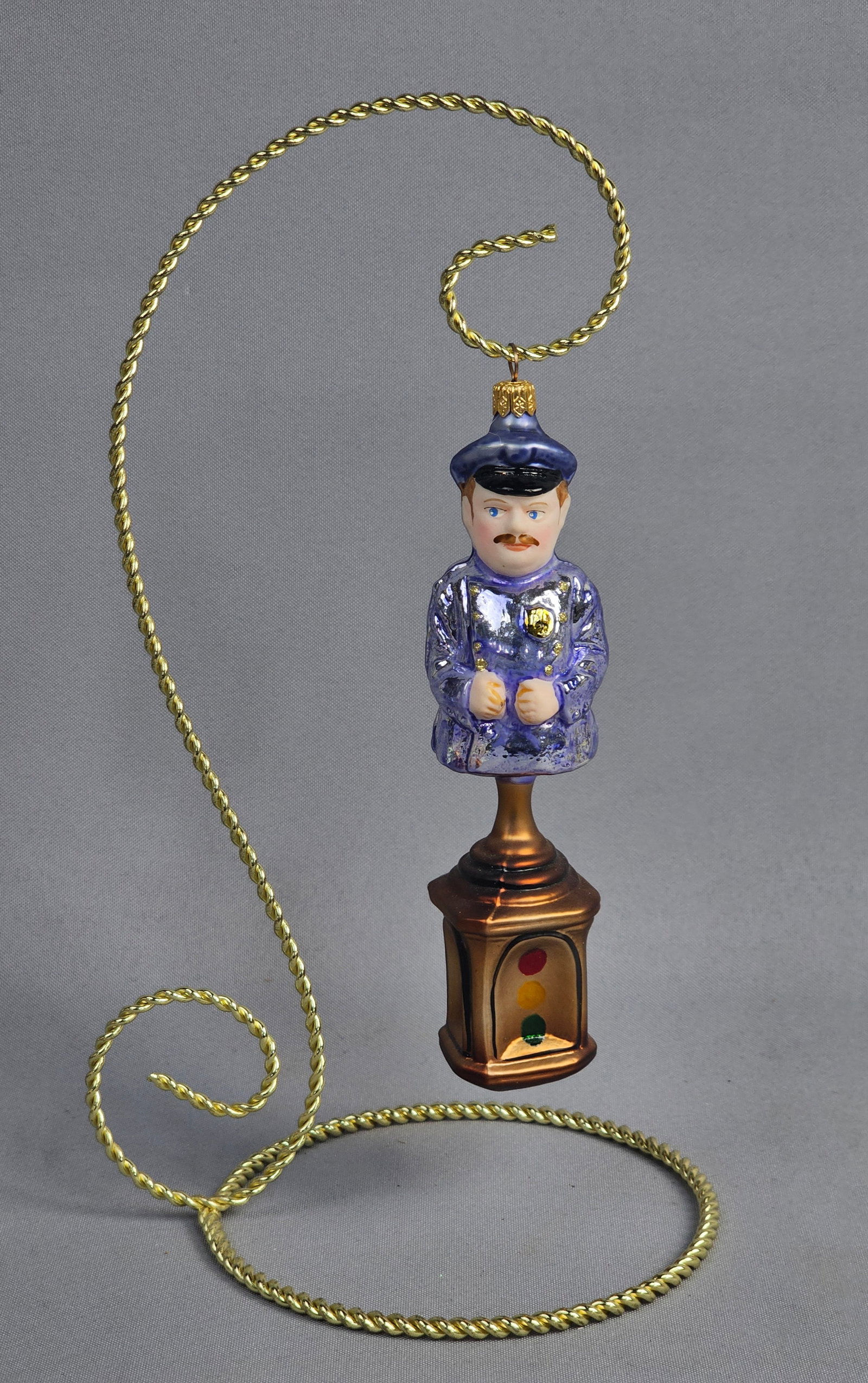 Joy to the World Polish Hand-Blown Glass Policeman on Traffic Light Ornament: Attributed to Joy to the World, this hand-blown glass Christmas ornament depicts a traffic officer standing atop a four-sided traffic signal pedestal. The figure is rendered in a light purple-blue iri