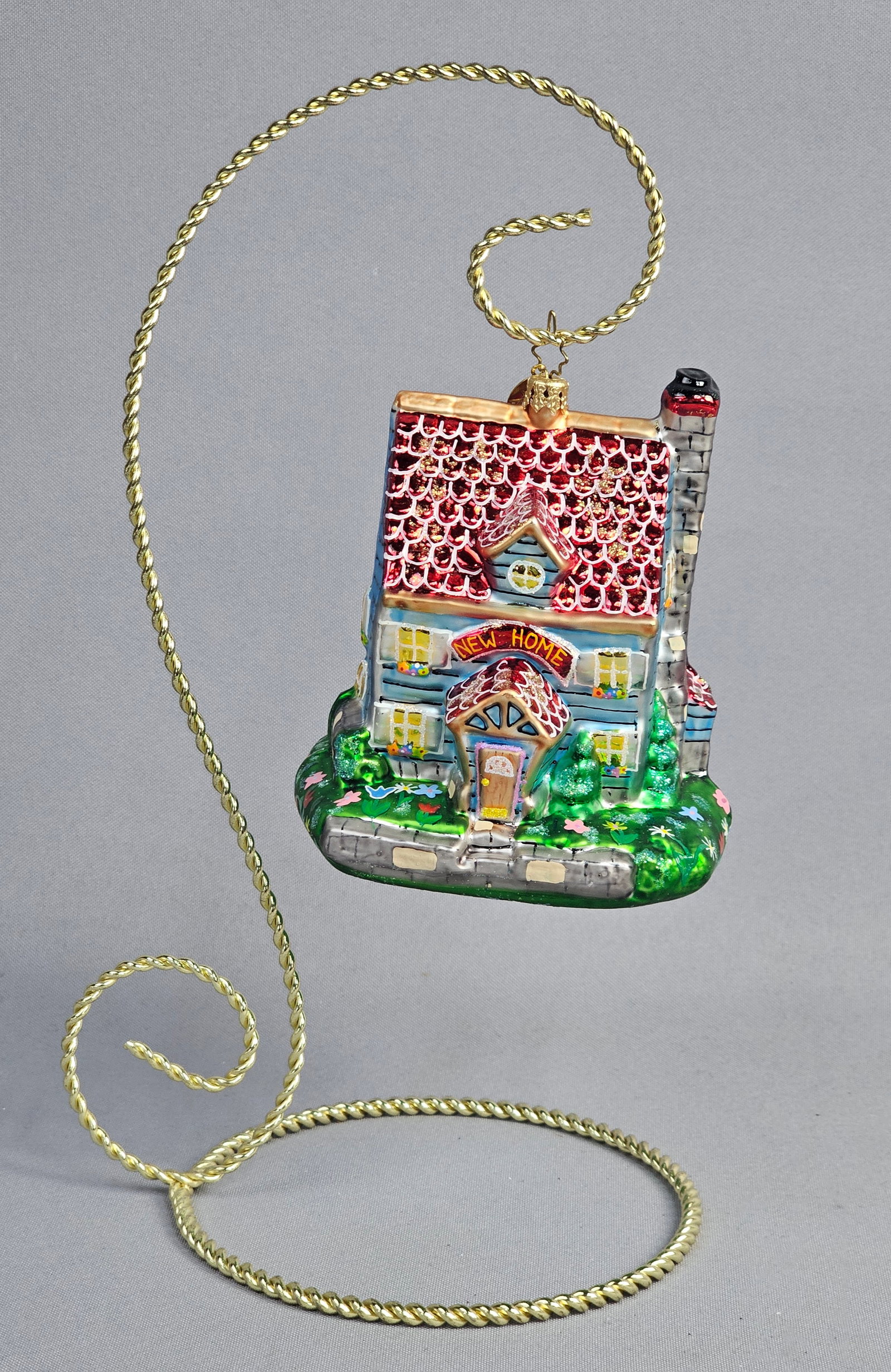 Christopher Radko Floral Cottage Charm New Home Glass Ornament: A mouth-blown, hand-painted glass Christmas ornament by Christopher Radko, titled Floral Cottage Charm. The ornament is shaped as a two-story house with blue horizontal siding and a steeply pitched re