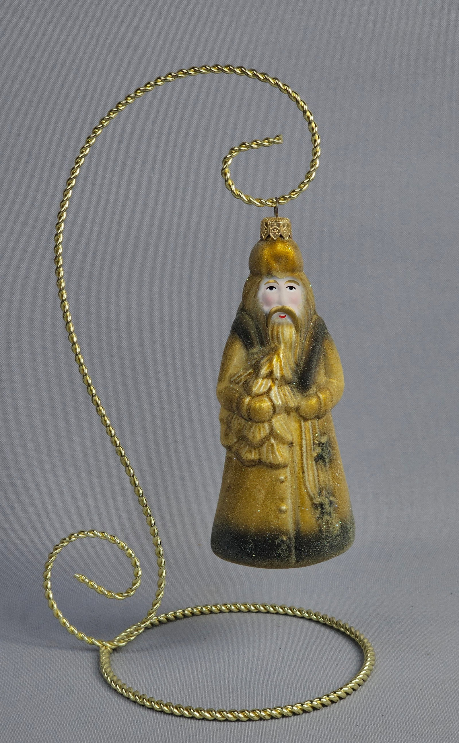 Christopher Radko Hand-Blown Glass Father Christmas Figure Ornament: A hand-blown glass Christmas ornament by Christopher Radko depicting a Father Christmas figure. The figure is modeled in a standing pose wearing a long robe featuring a color palette of golden-yellow 