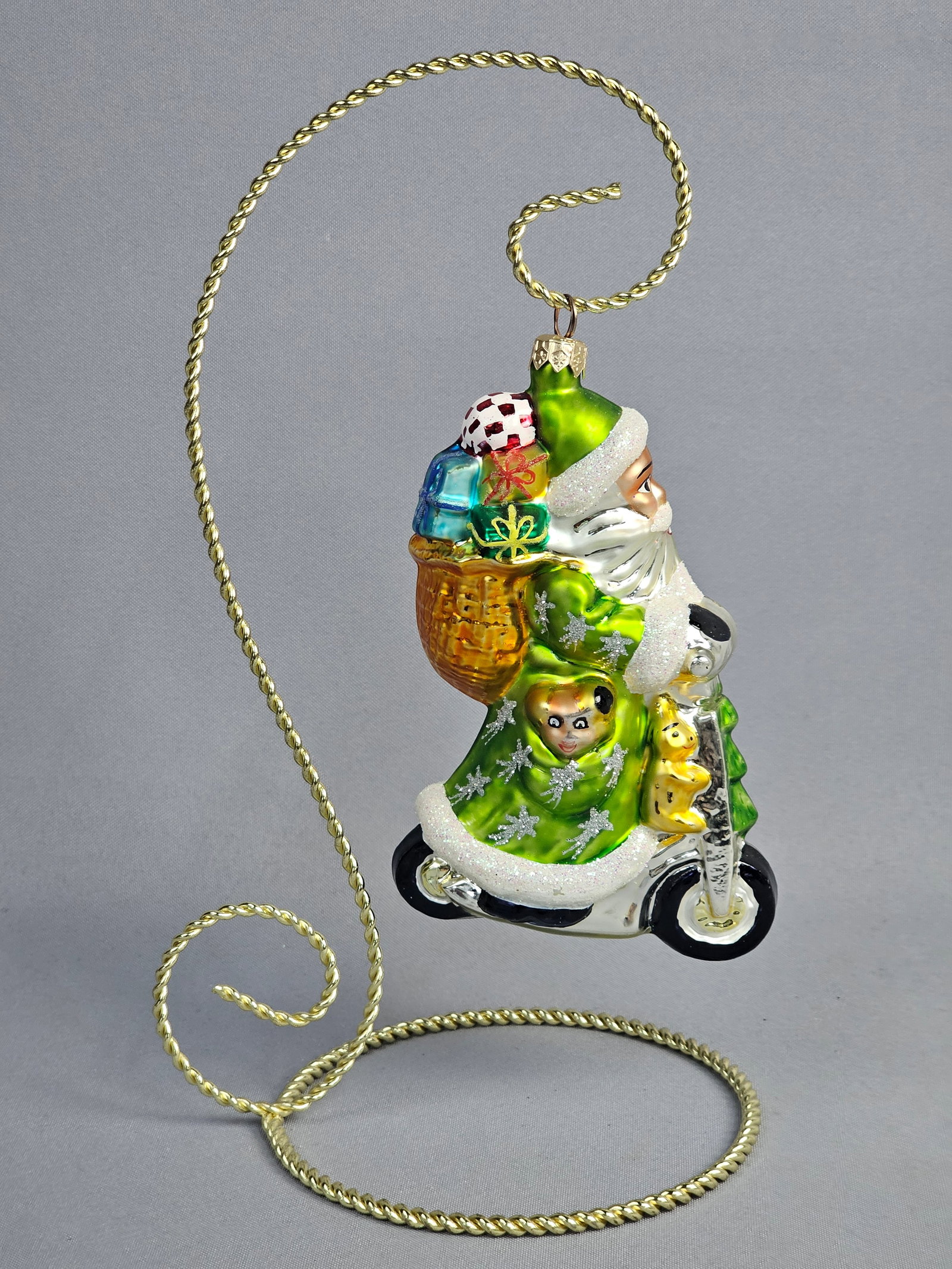Komozja Polish Hand-Blown Glass Santa Claus on Motorcycle Christmas Ornament: This mouth-blown and hand-painted glass Christmas ornament is manufactured by Komozja in Poland. The piece depicts Santa Claus in a non-traditional vibrant green coat with white glitter trim and silve