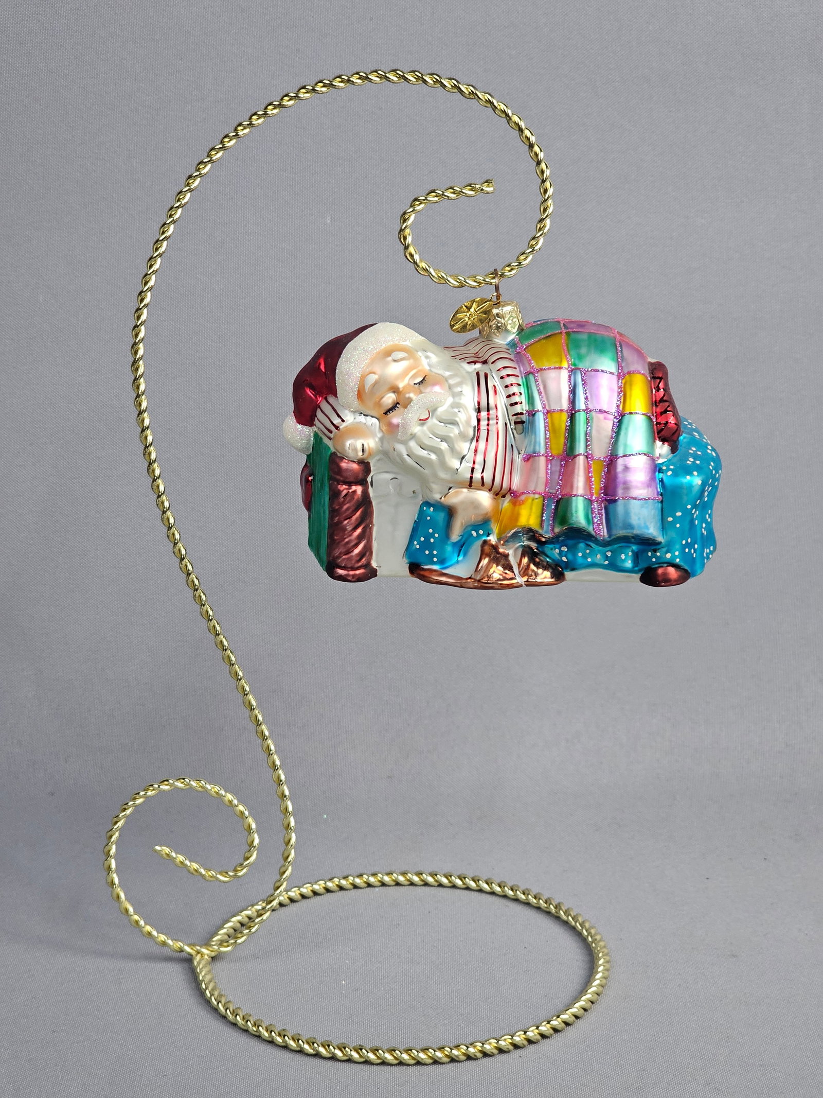Christopher Radko Sleeping Santa on Sofa Glass Christmas Ornament: A Christopher Radko hand-blown glass Christmas ornament featuring Santa Claus sleeping on a sofa. The figure is depicted wearing red and white striped pajamas and a red nightcap while holding a small 