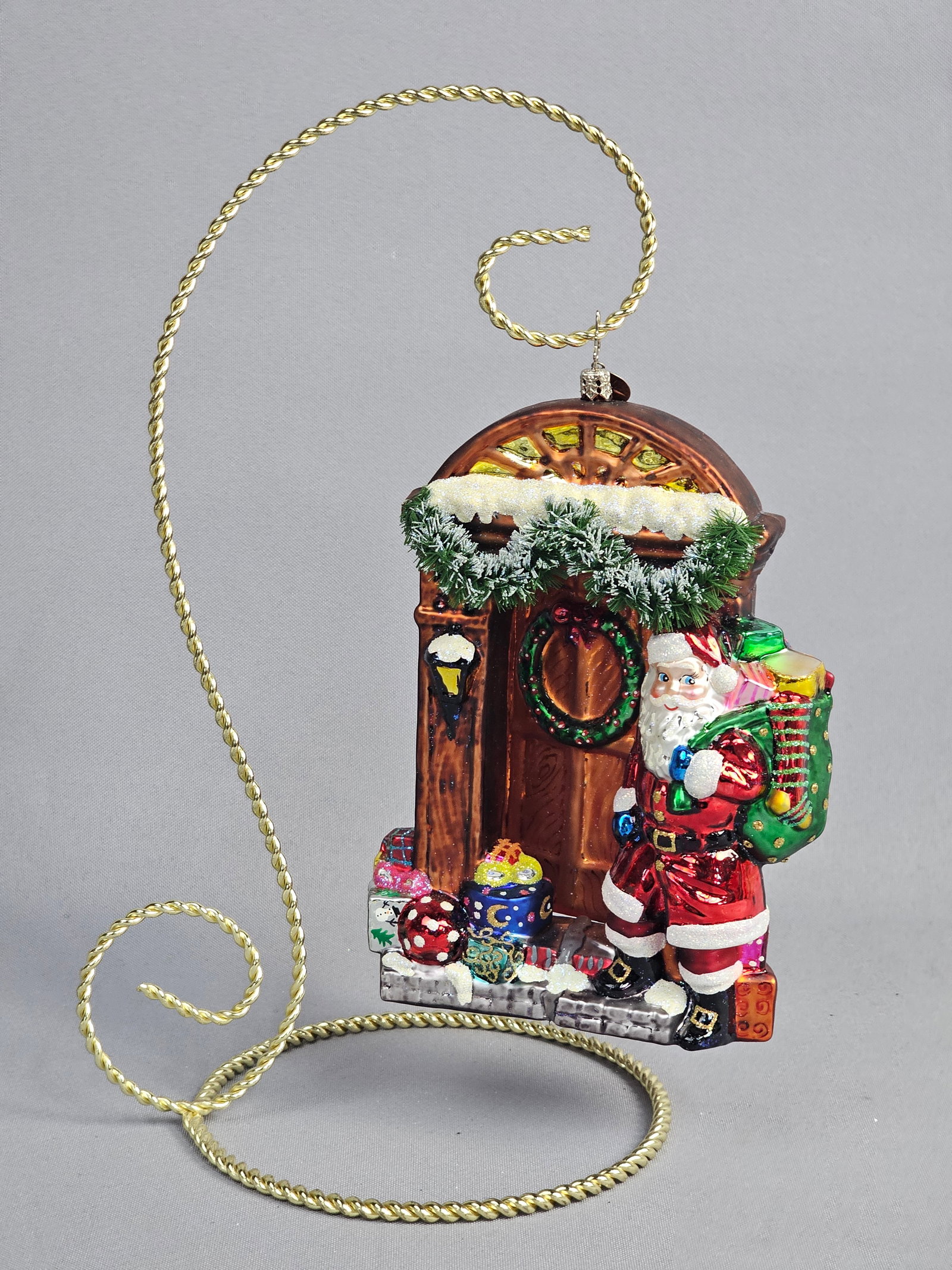 Christopher Radko Santas Sugary Abode Glass Christmas Ornament: This hand-blown glass Christmas ornament, identified as Santas Sugary Abode from Christopher Radko, features a Santa Claus figure in a red suit with a green toy sack standing beside a translucent ambe