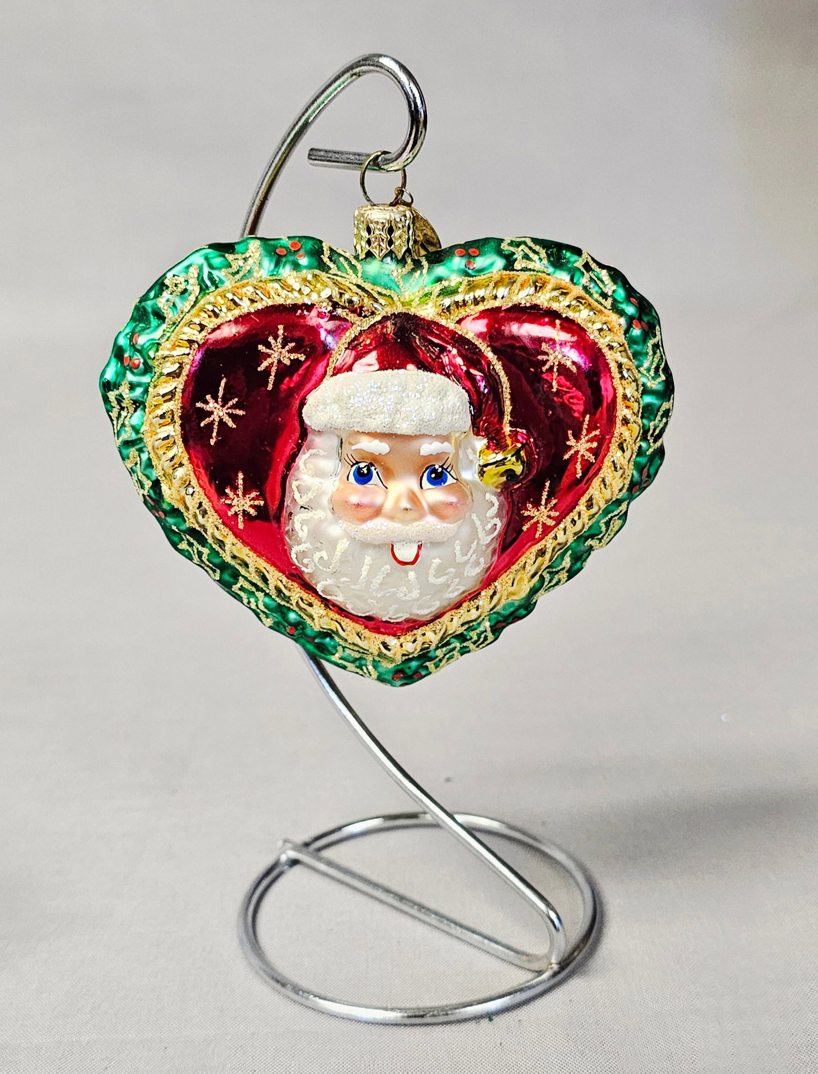 Christopher Radko Heart-Shaped Glass Ornament: Stand not included. A double-sided, mold-blown glass heart-shaped Christmas ornament by Christopher Radko. The ornament features a deep metallic red ground on both sides, accented with gold-toned glit