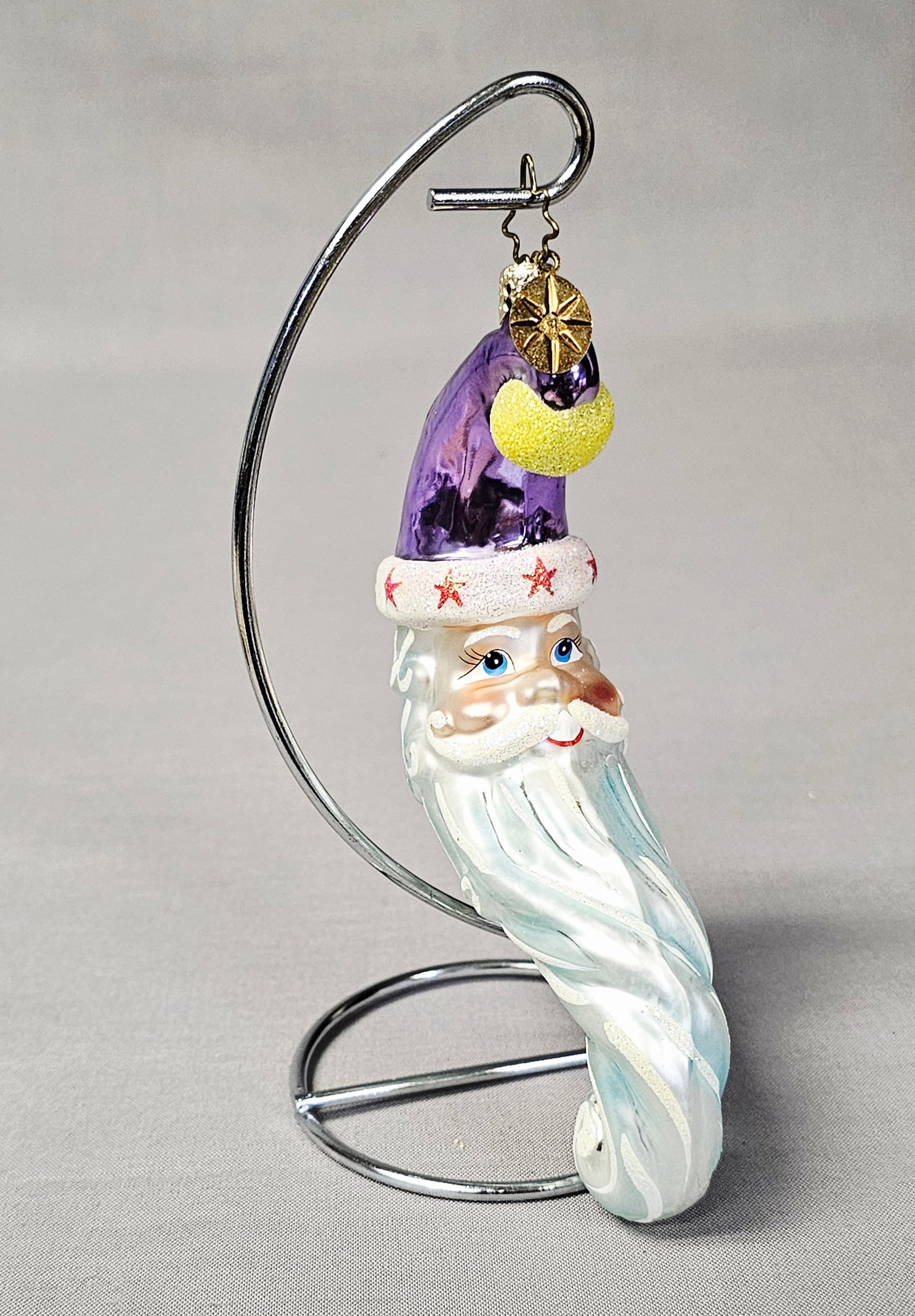Christopher Radko Enchanter Glass Santa Christmas Ornament: Stand not included. Christopher Radko Enchanter hand-blown glass Christmas ornament. This stylized Father Christmas figure features a tall, metallic purple pointed hat accented by a yellow glittered p