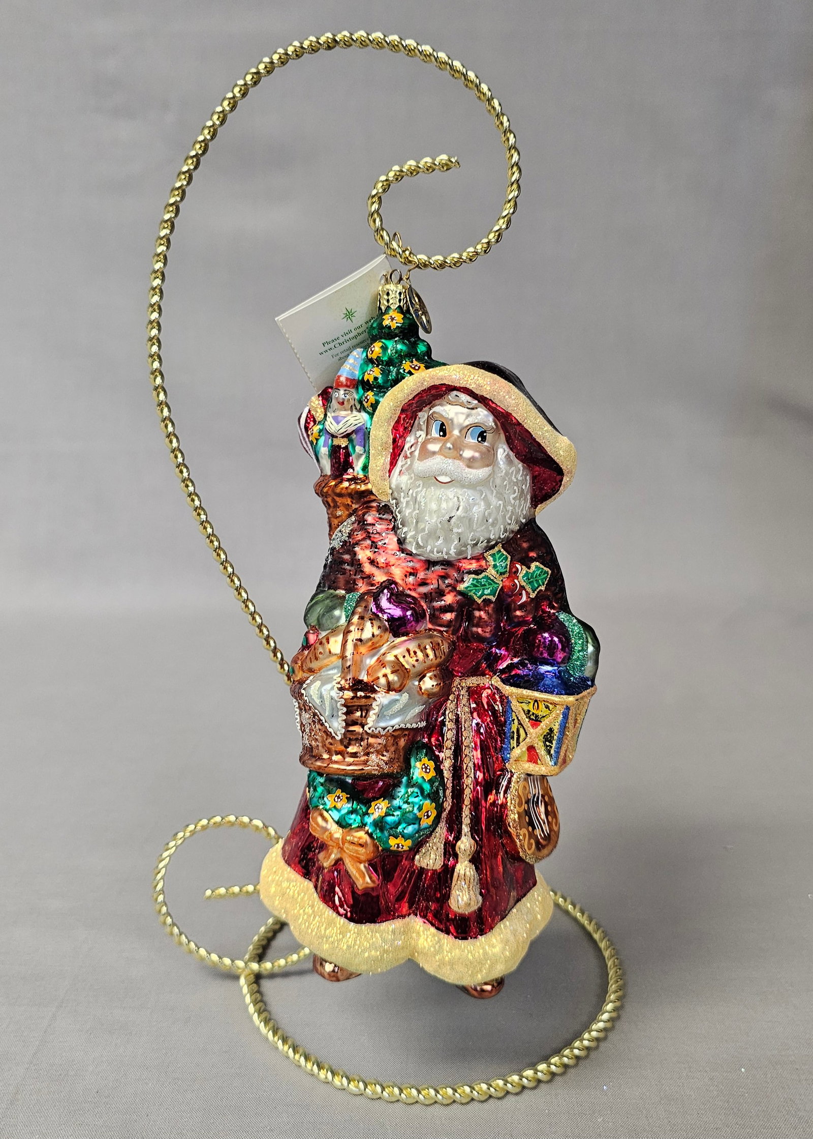 Christopher Radko Santa Provencal Glass Ornament: Stand not included. This figurative glass Christmas ornament is produced by Christopher Radko as part of the Santa through the Centuries collection, titled Santa Provencale. The piece represents a 12t