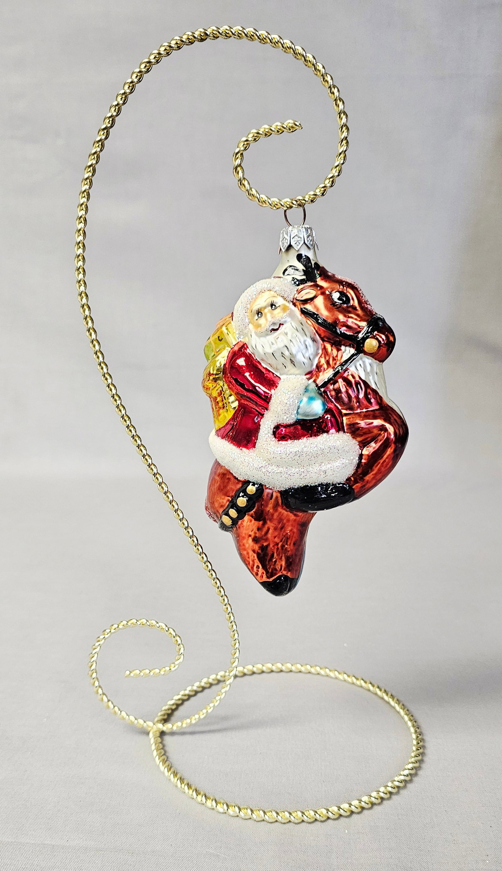 Christopher Radko Glass Santa on Reindeer Ornament: Stand not included. A mouth-blown glass Christmas ornament produced by Christopher Radko, featuring a Santa Claus figure riding a reindeer. The piece includes a silver-toned metal cap embossed with RA