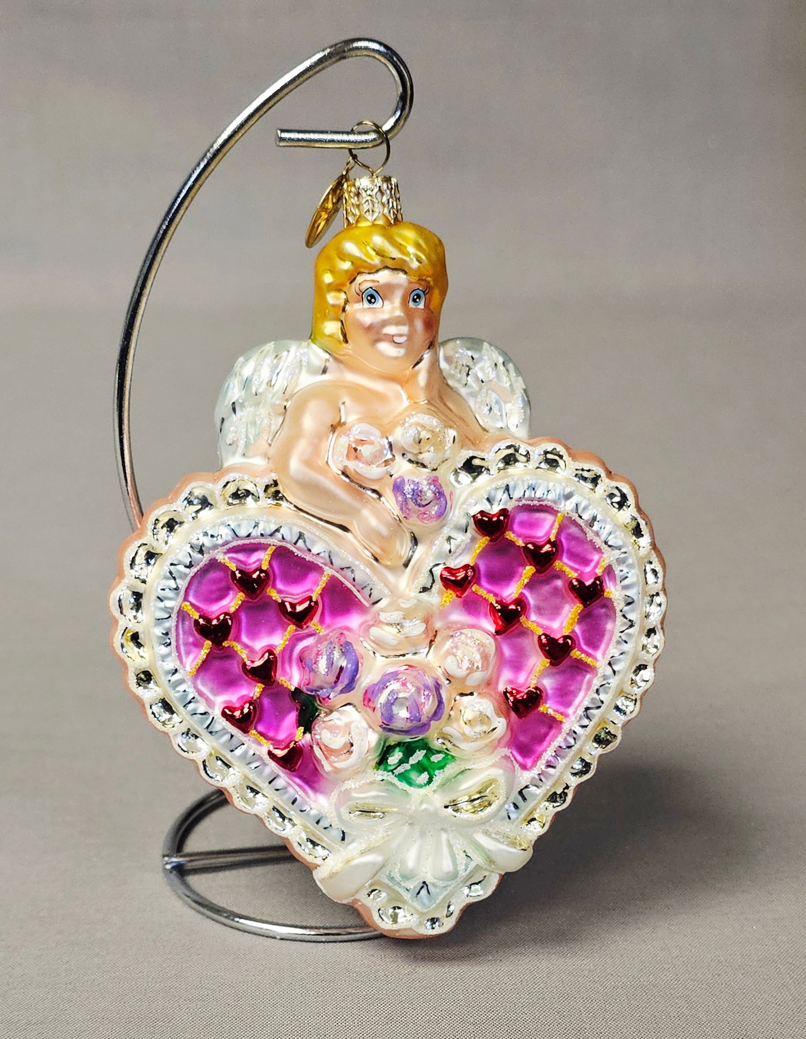 Christopher Radko Cupids Surprise Glass Heart Ornament: Stand not included. This holiday ornament is a retired Christopher Radko design titled Cupids Surprise, model number 02-0105-0. The piece is crafted from hand-blown glass and finished with hand-painte