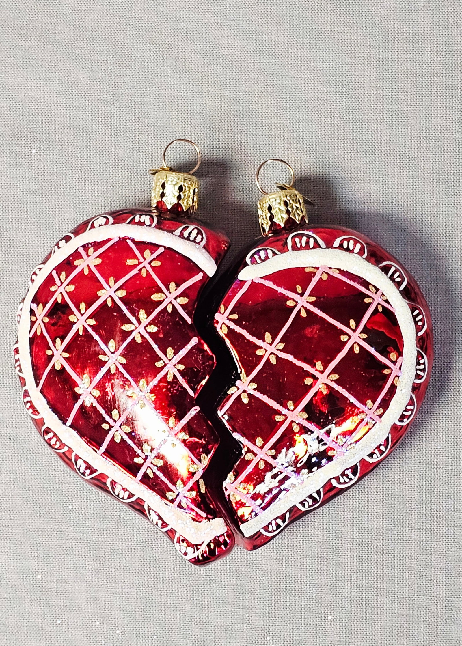 A Pair of Christopher Radko Glass Broken Heart Christmas Ornaments: A pair of mouth-blown glass Christmas ornaments by Christopher Radko, featuring a broken heart design. The two separate pieces are crafted from translucent red glass, hand-decorated with a white latti