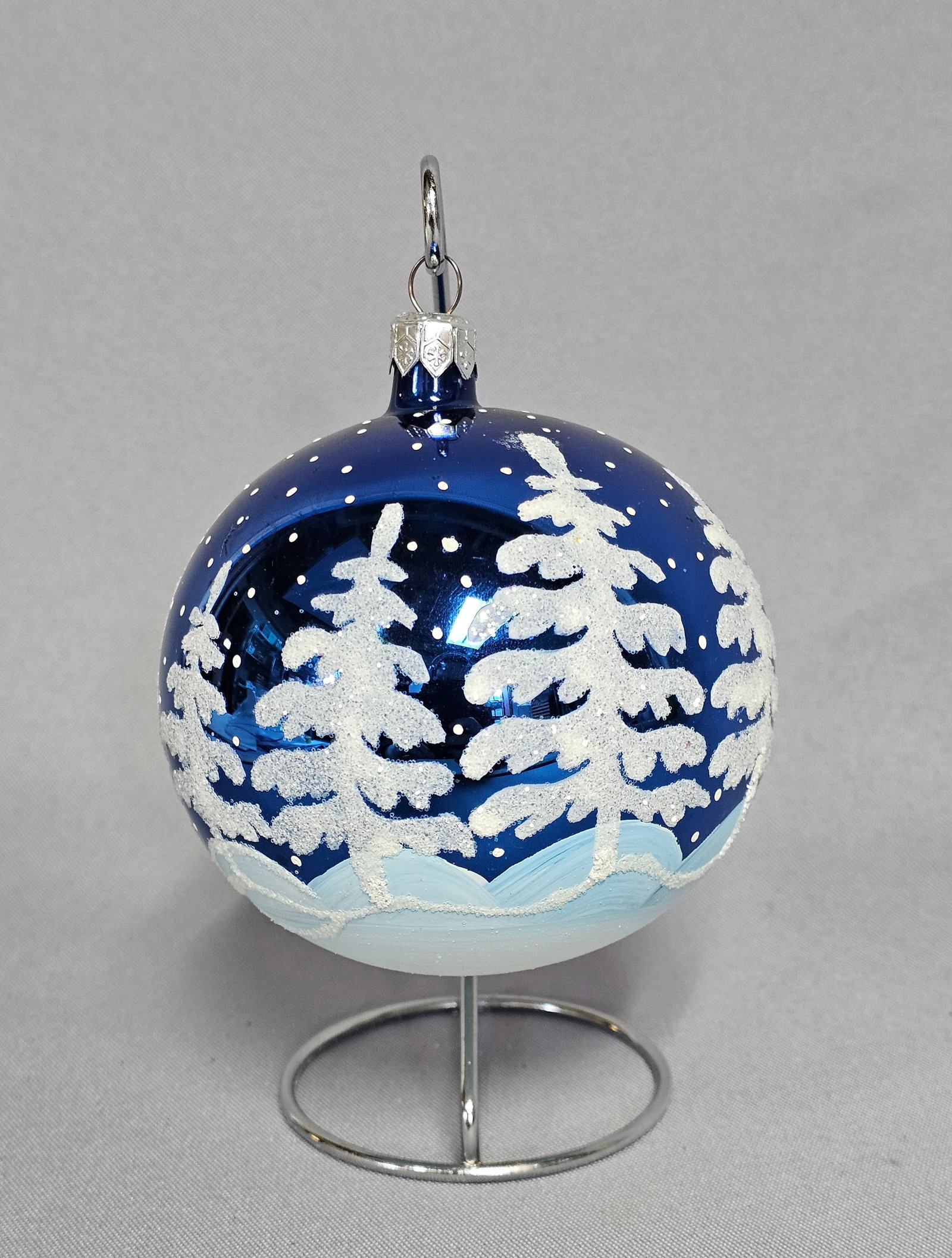 Christopher Radko Hand-Painted Blown Glass Cobalt Blue Winter Forest Christmas Ornament: A hand-painted blown glass Christmas ornament produced by Christopher Radko. The ornament is a spherical cobalt blue glass bauble featuring a hand-decorated winter forest scene. The design includes st
