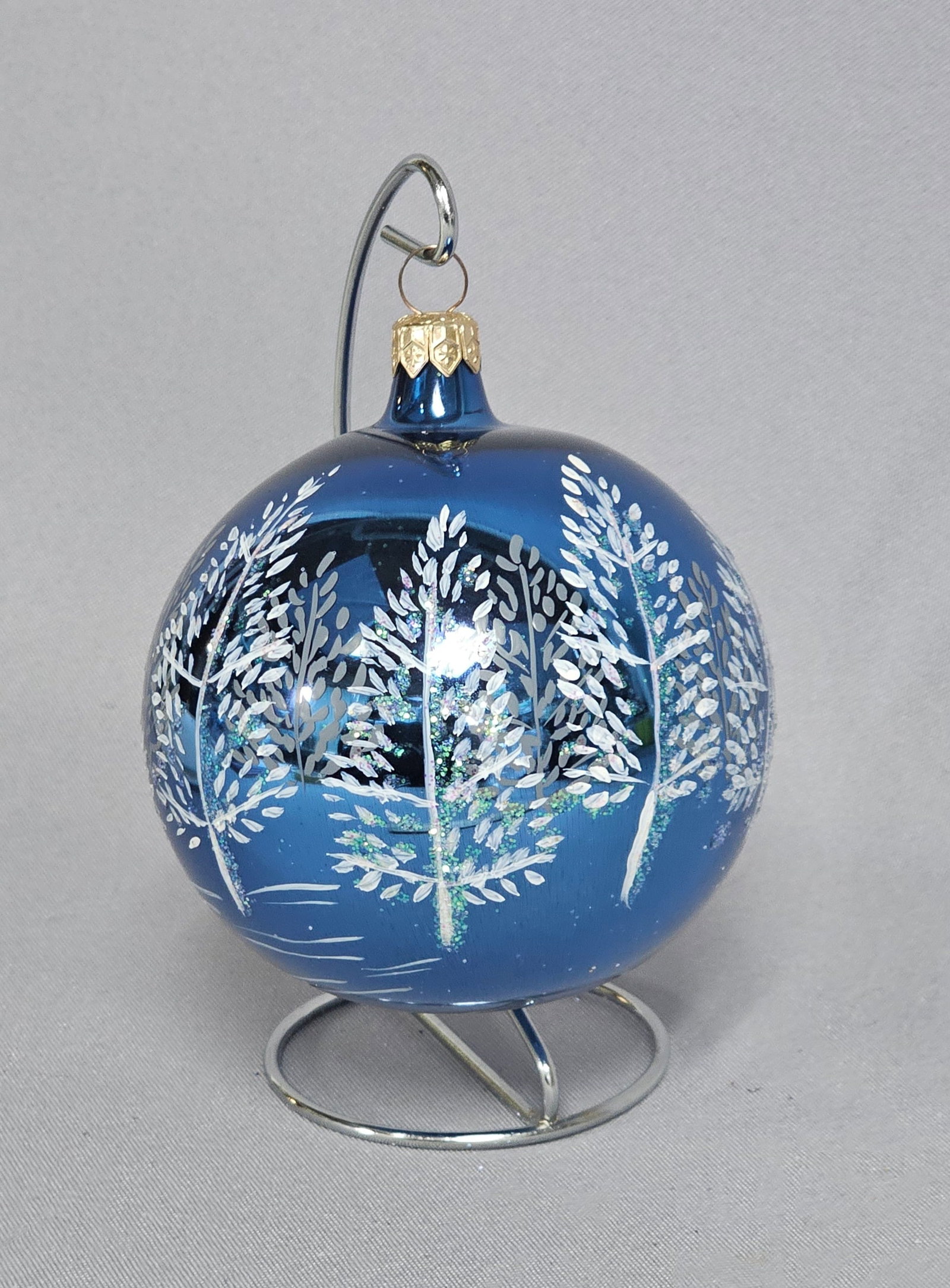 Polish Hand-Painted Cobalt Blue Blown Glass Christmas Ball Ornament: This spherical Christmas ornament is crafted from hand-blown glass with a deep cobalt blue finish. The exterior features a hand-painted winter forest scene composed of stylized trees rendered in textu