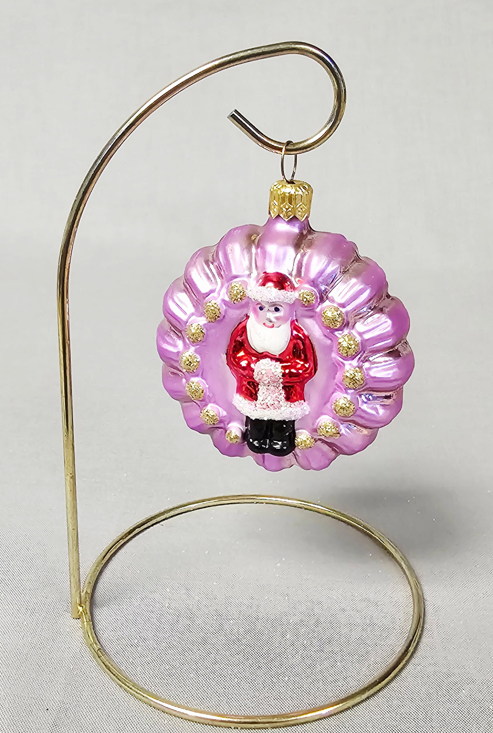 Christopher Radko Glass Santa Reflector Ornament: Stand not included. A mouth-blown glass Christmas ornament by Christopher Radko. This circular, fluted saucer-shaped disc is made of mercury glass with a metallic lavender-pink finish. The obverse fea