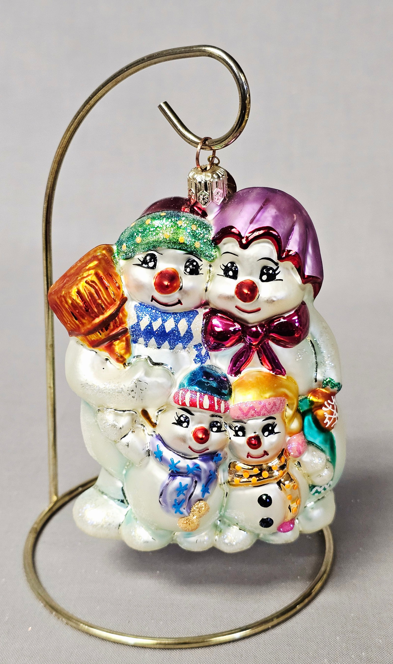 Christopher Radko Glass Snowman Family Ornament: Stand not included. This mouth-blown and hand-painted glass Christmas ornament is produced by Christopher Radko. The design features a family of four snowmen posed together on a glittered snow base. H
