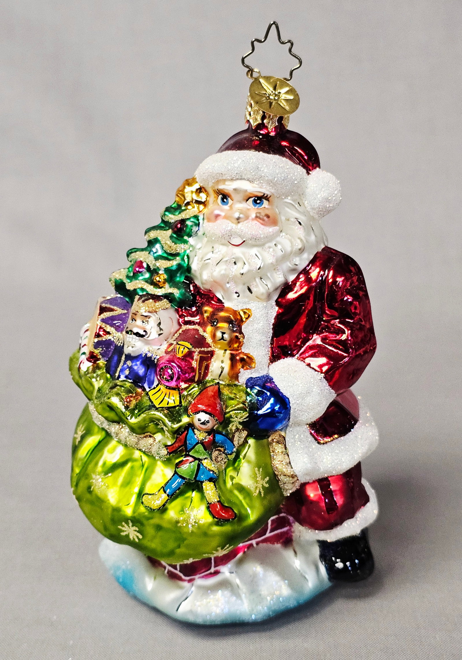 Christopher Radko Santa Claus with Toy Sack Ornament: This hand-blown glass Christmas ornament is attributed to Christopher Radko and depicts Santa Claus in a traditional red metallic suit with white glitter trim and blue mittens. The ornament is in exce