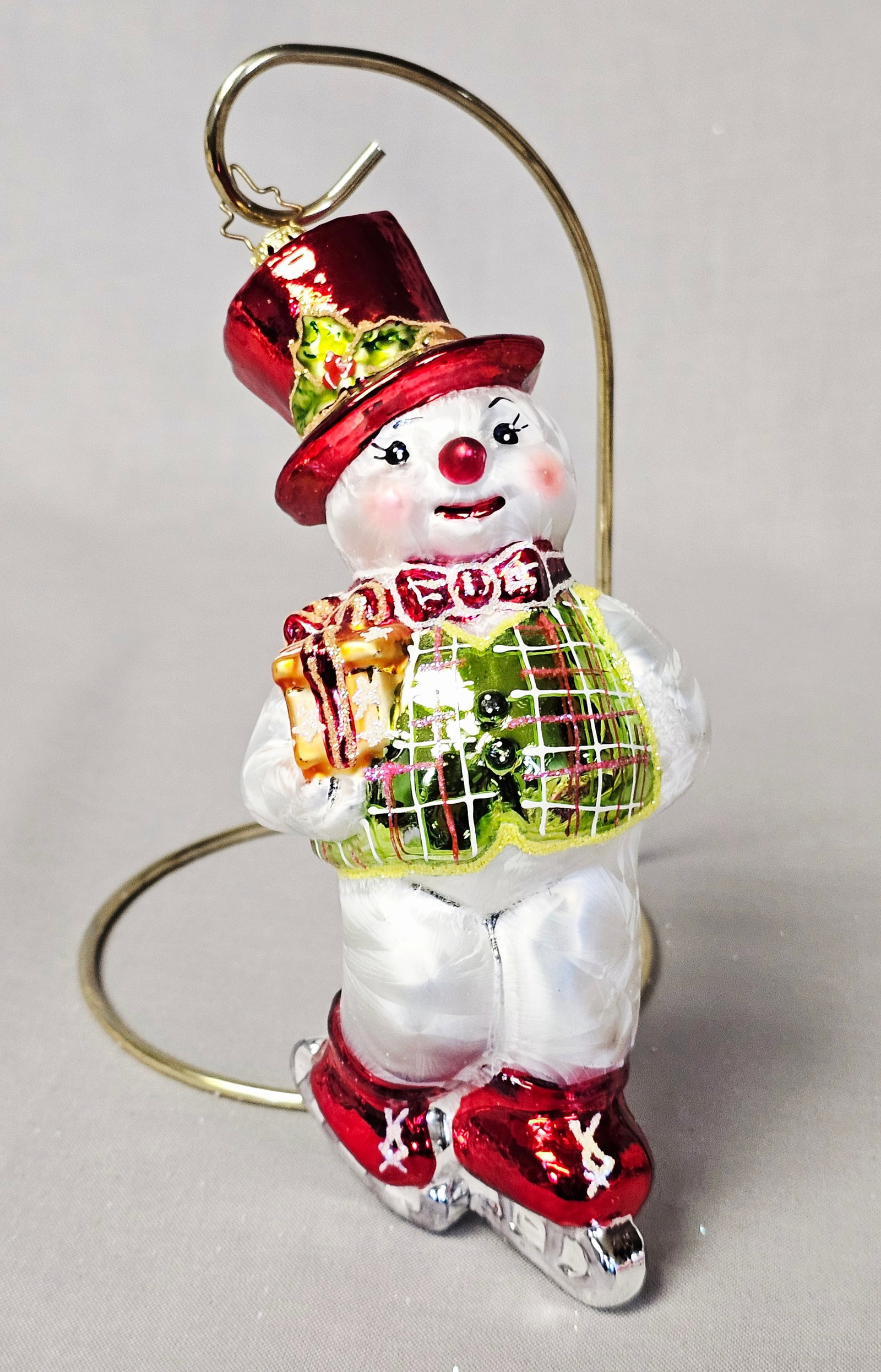 Christopher Snowman Ice Skating Glass Ornament: Stand not included. This is a handcrafted glass Christmas ornament designed by Christopher Radko. The ornament depicts a whimsical snowman in a dynamic ice-skating pose. He is dressed in a festive out