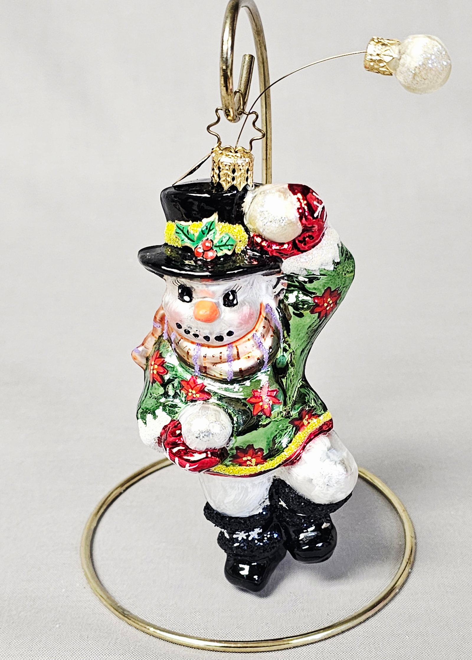 Christopher Radko Glass Snowman Ornament: Stand not included. A hand-blown glass Christmas ornament manufactured by Christopher Radko. The figure depicts a snowman in a dynamic pose, holding a glittered snowball in one hand with a second snow