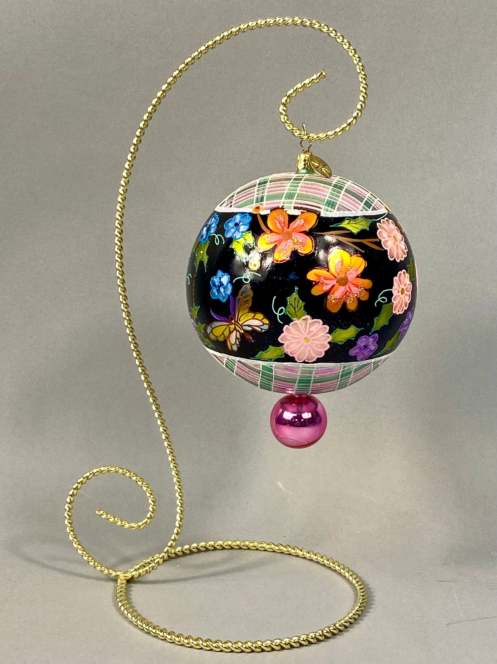 Radko Hand-Painted Glass Ornament: The spherical ornament features a wide central band of black finish decorated with various multi-colored floral blossoms and butterflies, further accented with fine glitter detailing. The top and bott