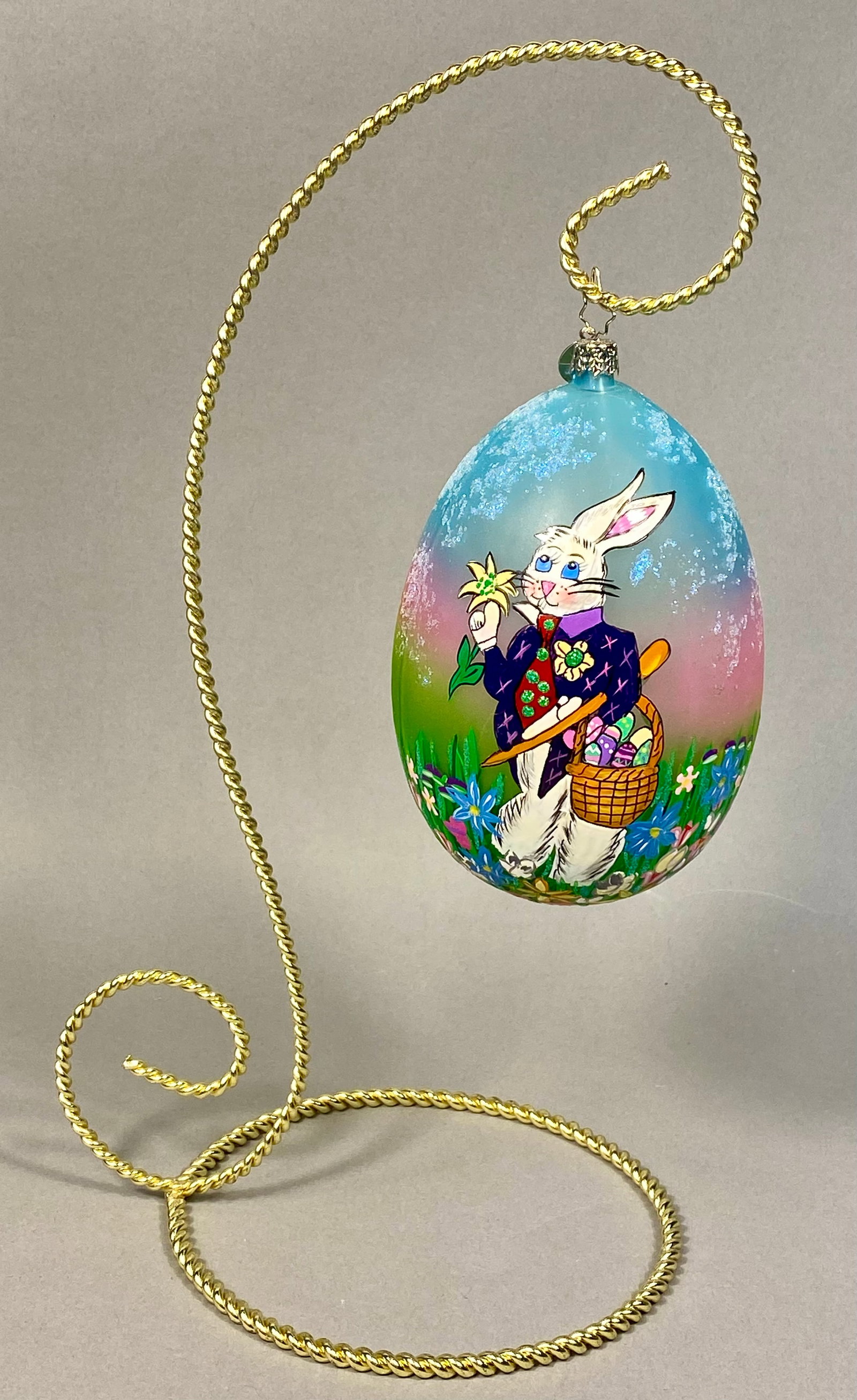 Radko Hand-Painted Glass Easter Rabbit Egg Ornament: A mouth-blown glass Easter egg ornament from Christopher Radko. The piece features a hand-painted scene of a dapper white rabbit dressed in a navy blue jacket, purple collar, yellow floral boutonniere
