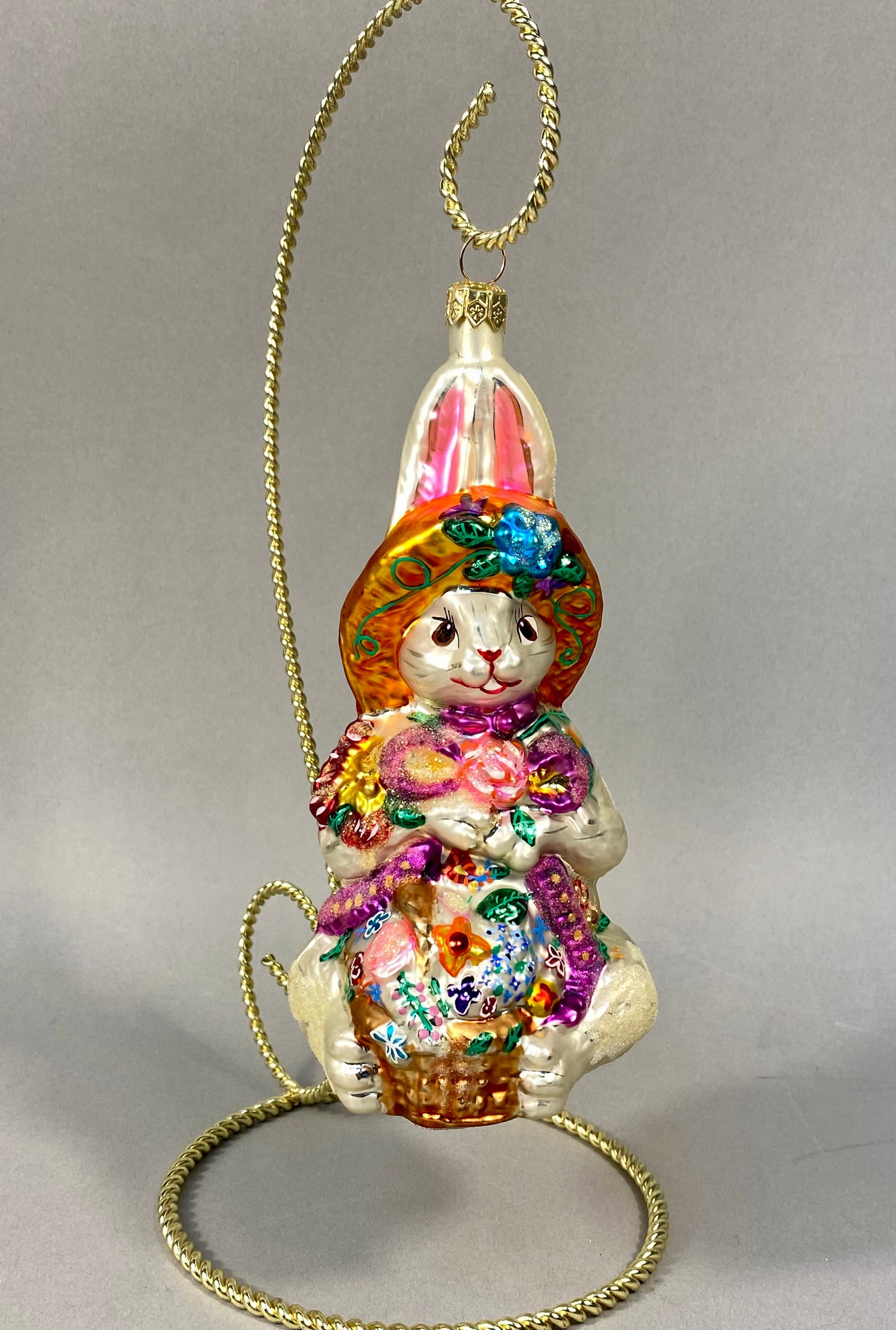 Radko Billy Bunny Goes Shopping Glass Ornament: Christopher Radko Billy Bunny Goes Shopping hand-blown glass ornament. This piece features a seated white rabbit wearing a wide-brimmed sun hat in a golden-orange hue, accented with a large blue flowe