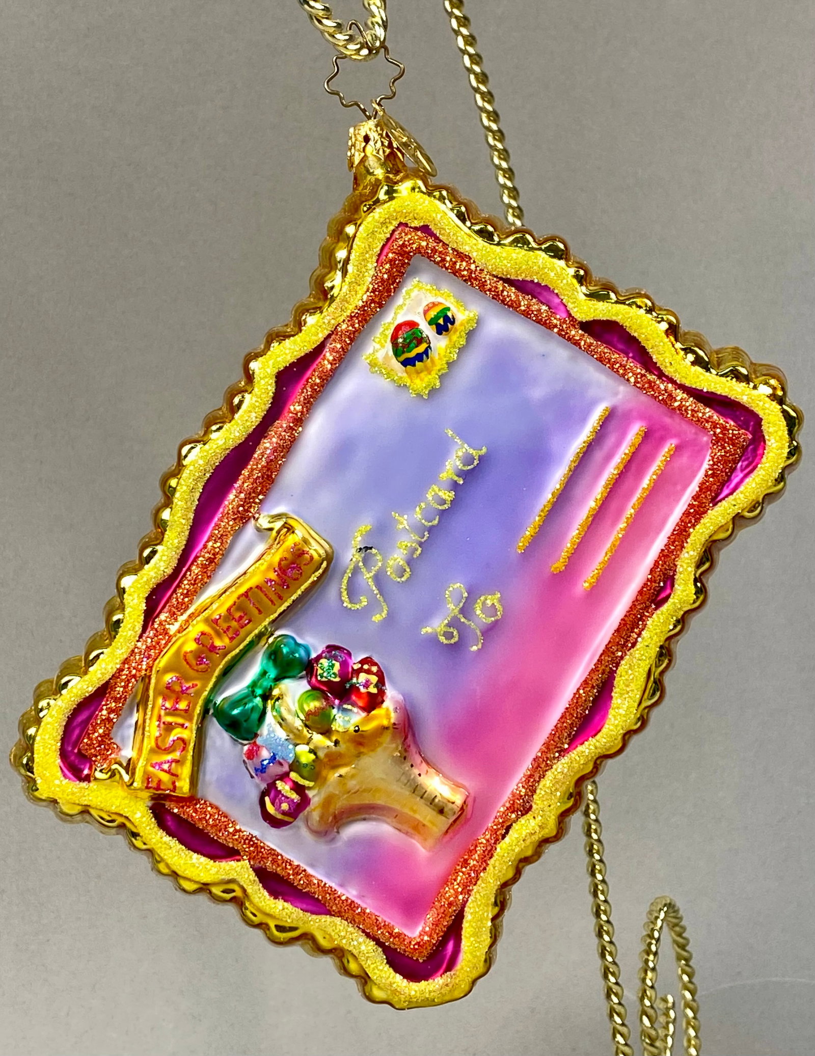Radko Postcards-Greetings Easter Glass Ornament: Hand-blown glass holiday ornament by Christopher Radko from the Postcards-Greetings series. The rectangular ornament is designed as a double-sided postcard with scalloped, gold-glittered edges. The or