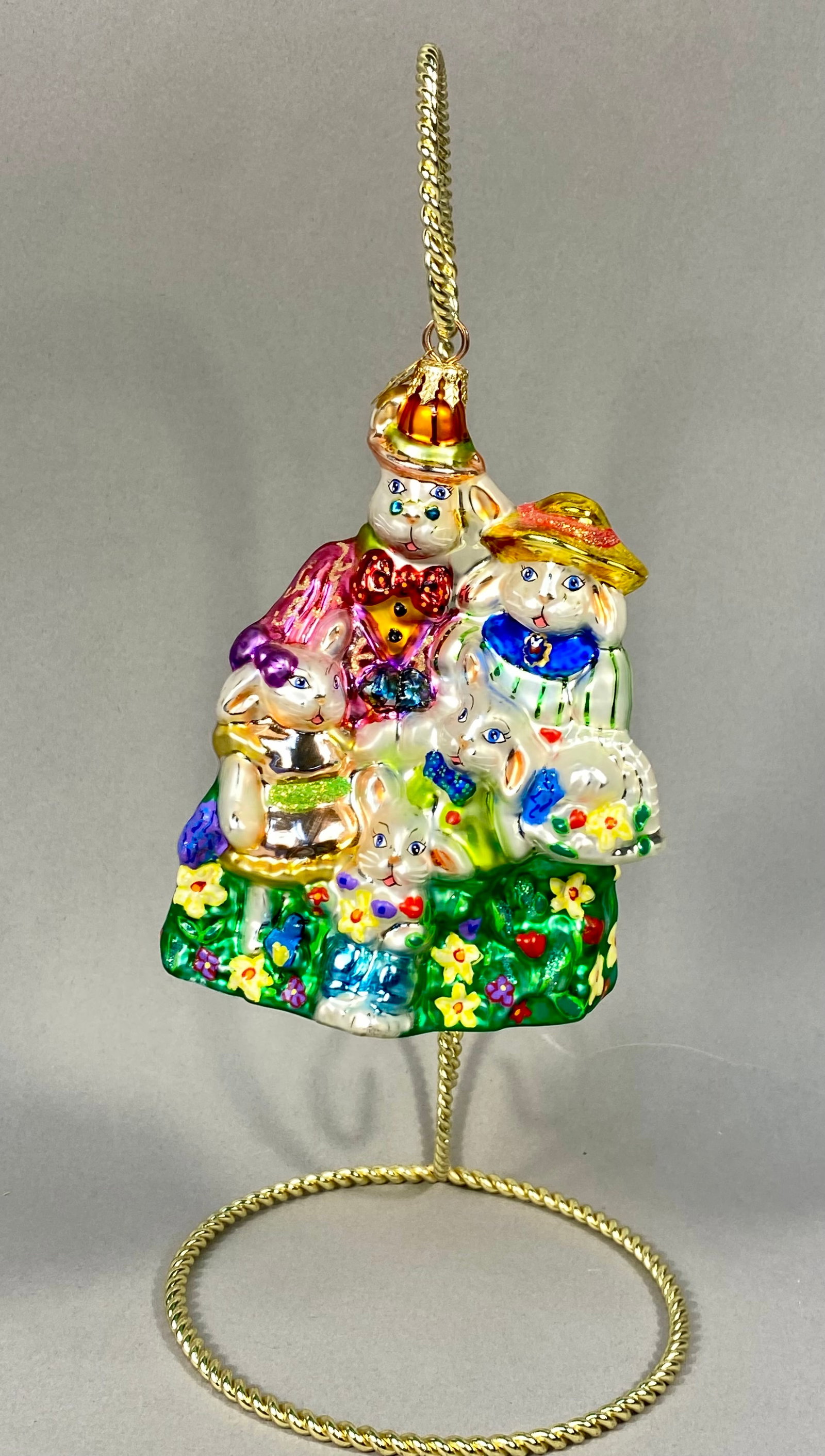 Radko Bunny Family Hand-Blown Glass Ornament: A Christopher Radko mouth-blown silvered glass ornament featuring a family of five rabbits in a garden setting. The piece is finished with hand-painted details and multicolored glitter accents. The go