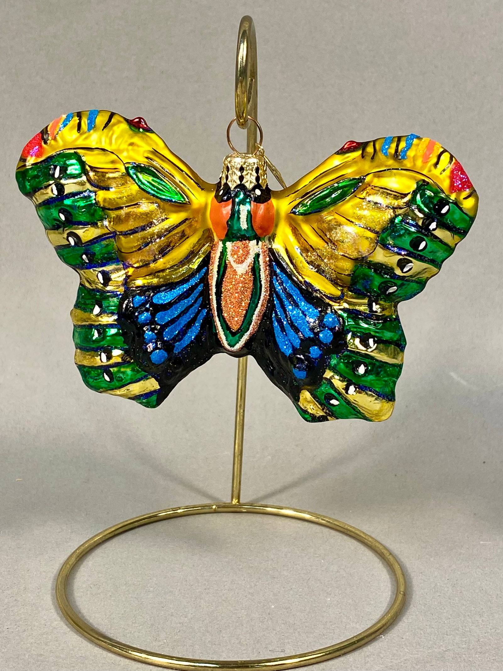 Radko Hand-Painted Blown Glass Butterfly Ornament: A hand-painted blown glass ornament by Christopher Radko, crafted in the form of a stylized butterfly. The ornament features a bright yellow ground on the wings, decorated with horizontal bands of eme