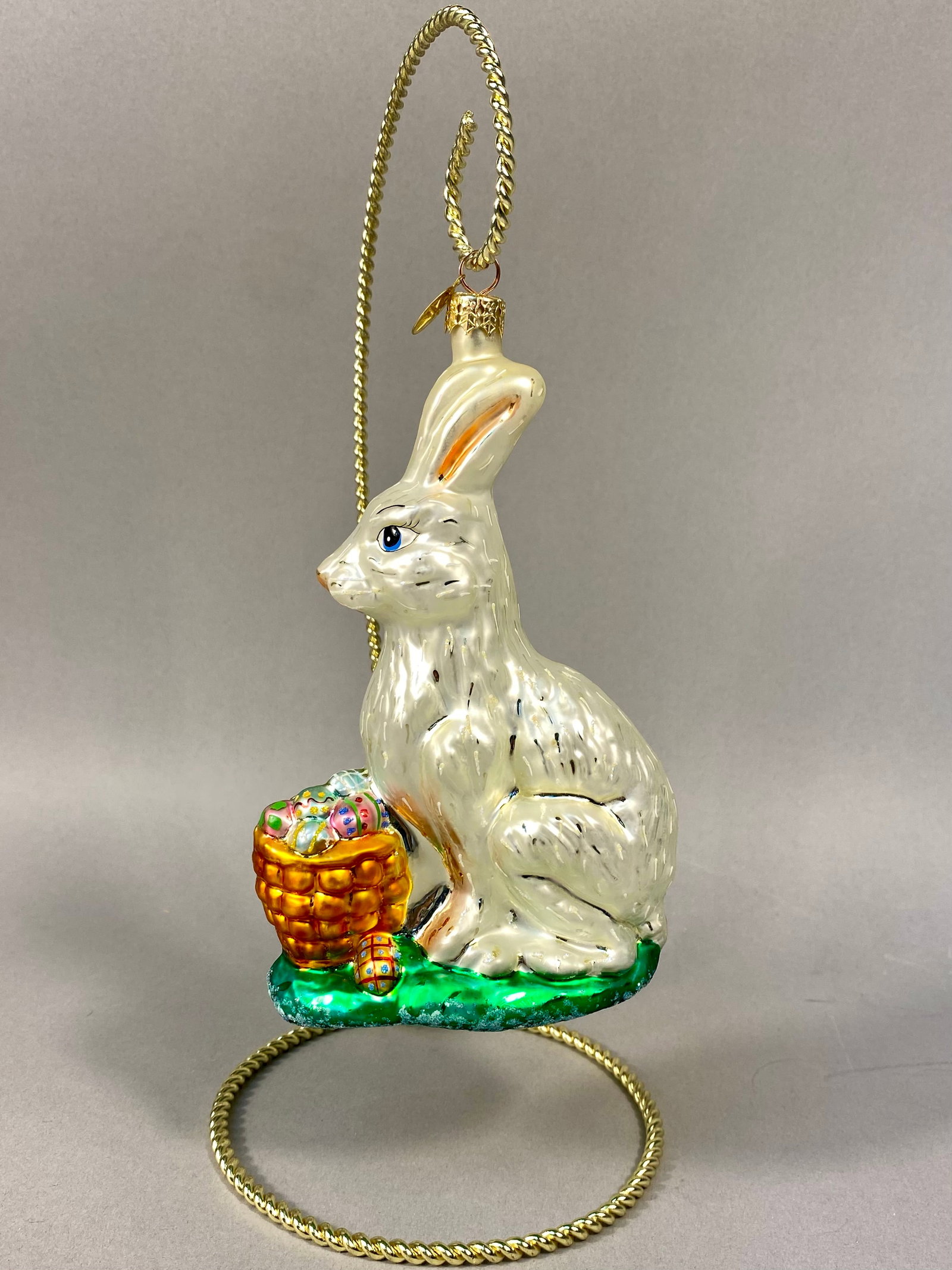 Radko Bunnytrail Basket Blown Glass Ornament: Christopher Radko hand-blown glass Easter ornament titled Bunnytrail Basket. The figurine depicts an upright rabbit with a pearlescent white iridescent finish and hand-painted details, including blue 