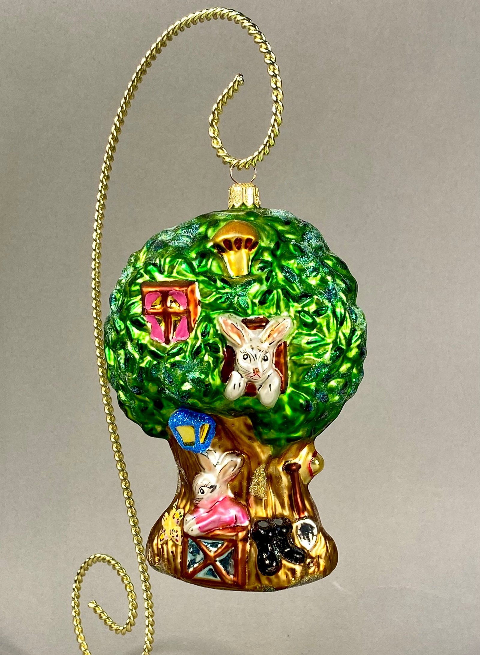 Radko Happy Hideaway Figural Glass Ornament: This is a mouth-blown figural glass ornament by Christopher Radko, identified as the Happy Hideaway design. The ornament is shaped like a whimsical treehouse for rabbits. The upper canopy is finished 
