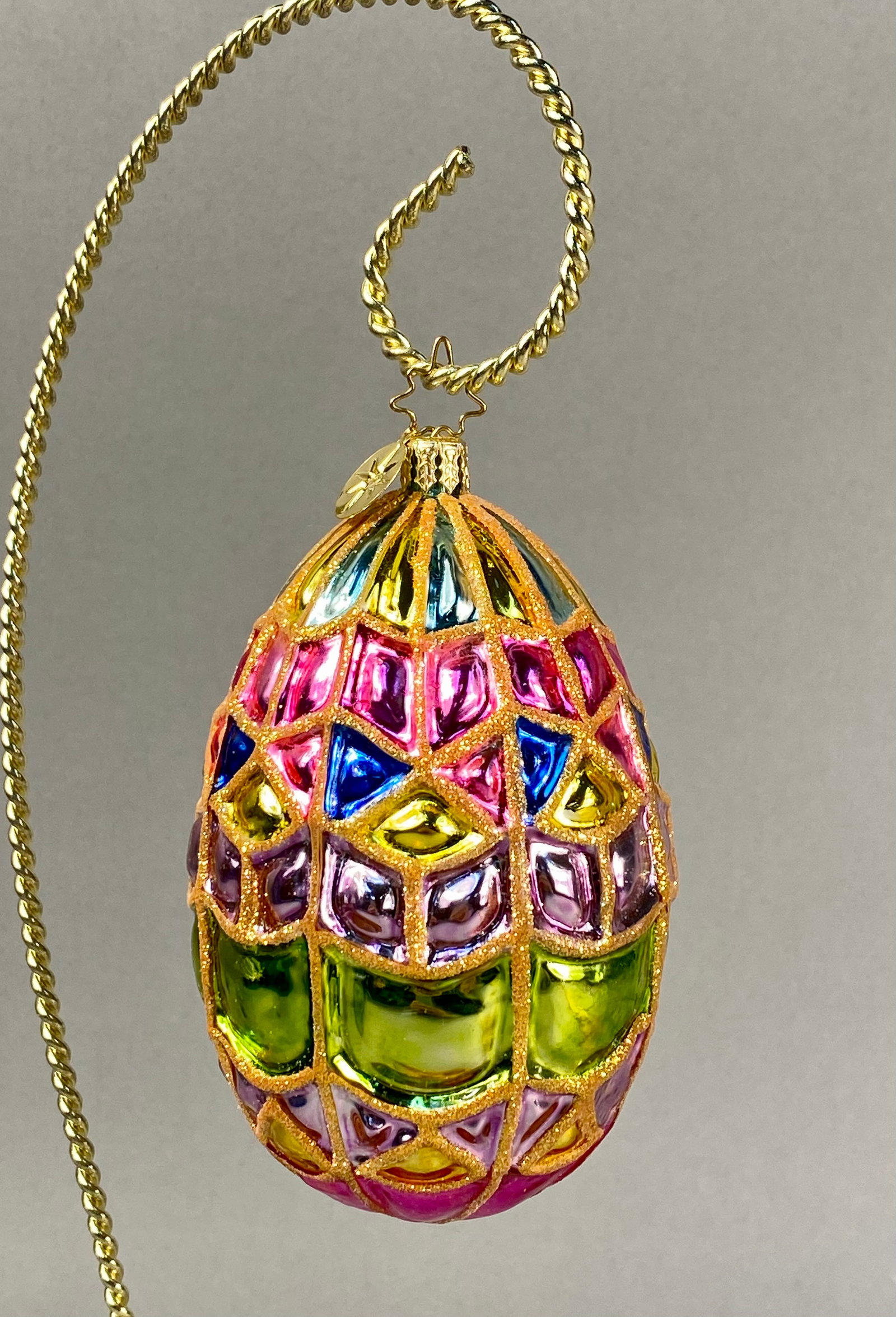 Radko Glass Mosaic Egg Ornament: A Christopher Radko mouth-blown glass ornament designed in the form of a decorative egg featuring a multi-colored mosaic or stained glass pattern. The surface is decorated with translucent segments in