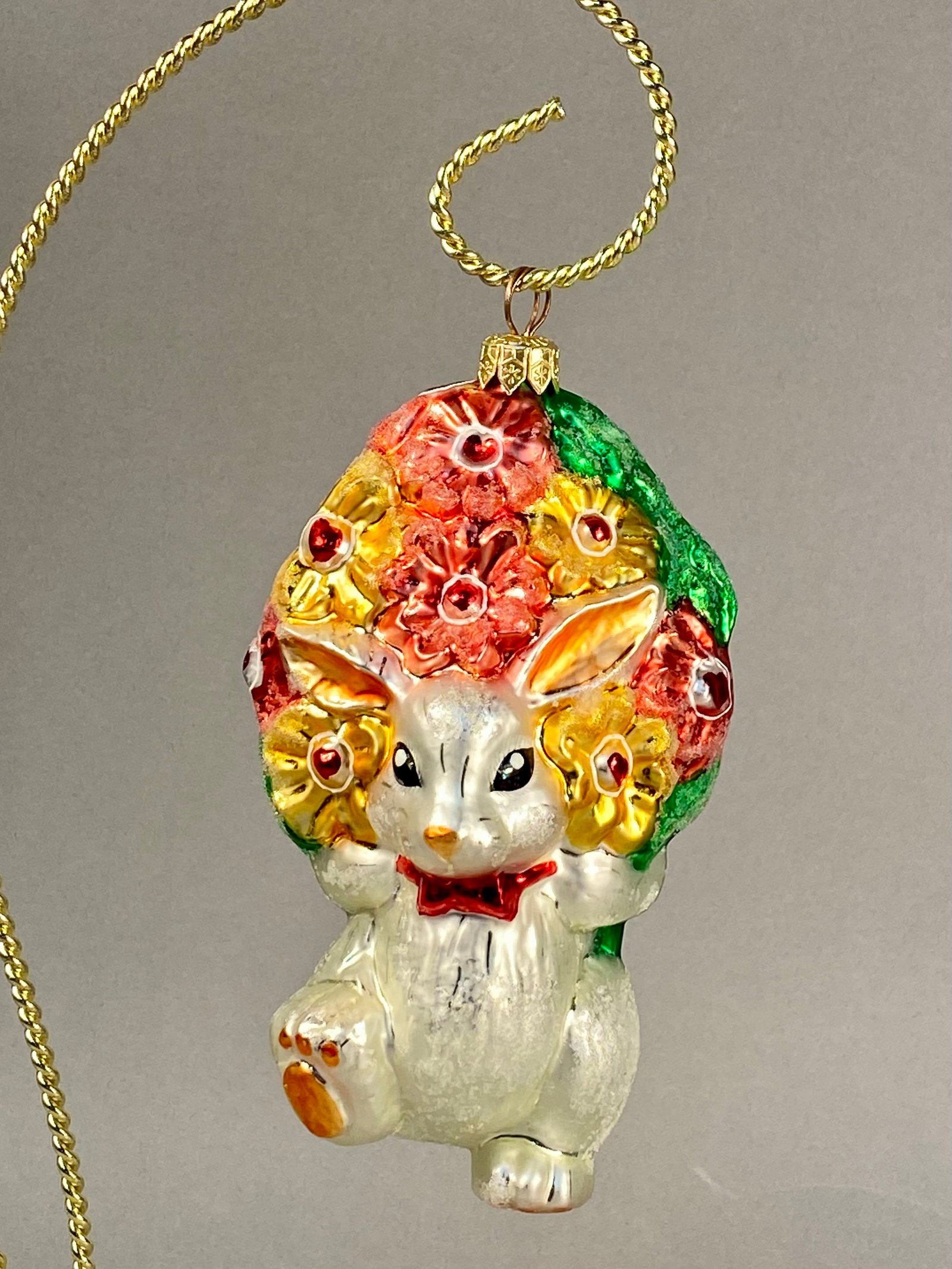 Radko Bringing You a Bunch of Love Bunny Ornament: This is a hand-blown glass holiday ornament by Christopher Radko, titled Bringing You a Bunch of Love. The ornament features a white rabbit with a pearlescent finish depicted in an upright pose with o