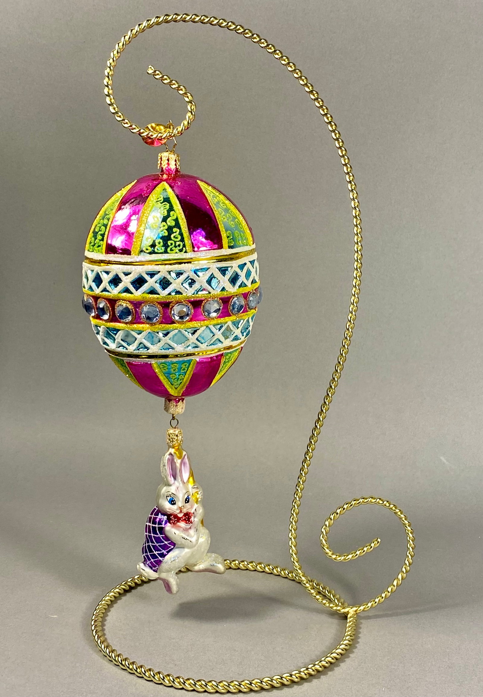 Radko Egg and Bunny Pendant Ornament: A large, two-part mouth-blown glass holiday ornament by Christopher Radko. The ornament features a substantial upper egg-shaped glass body decorated with vibrant panels of metallic hot pink and light 