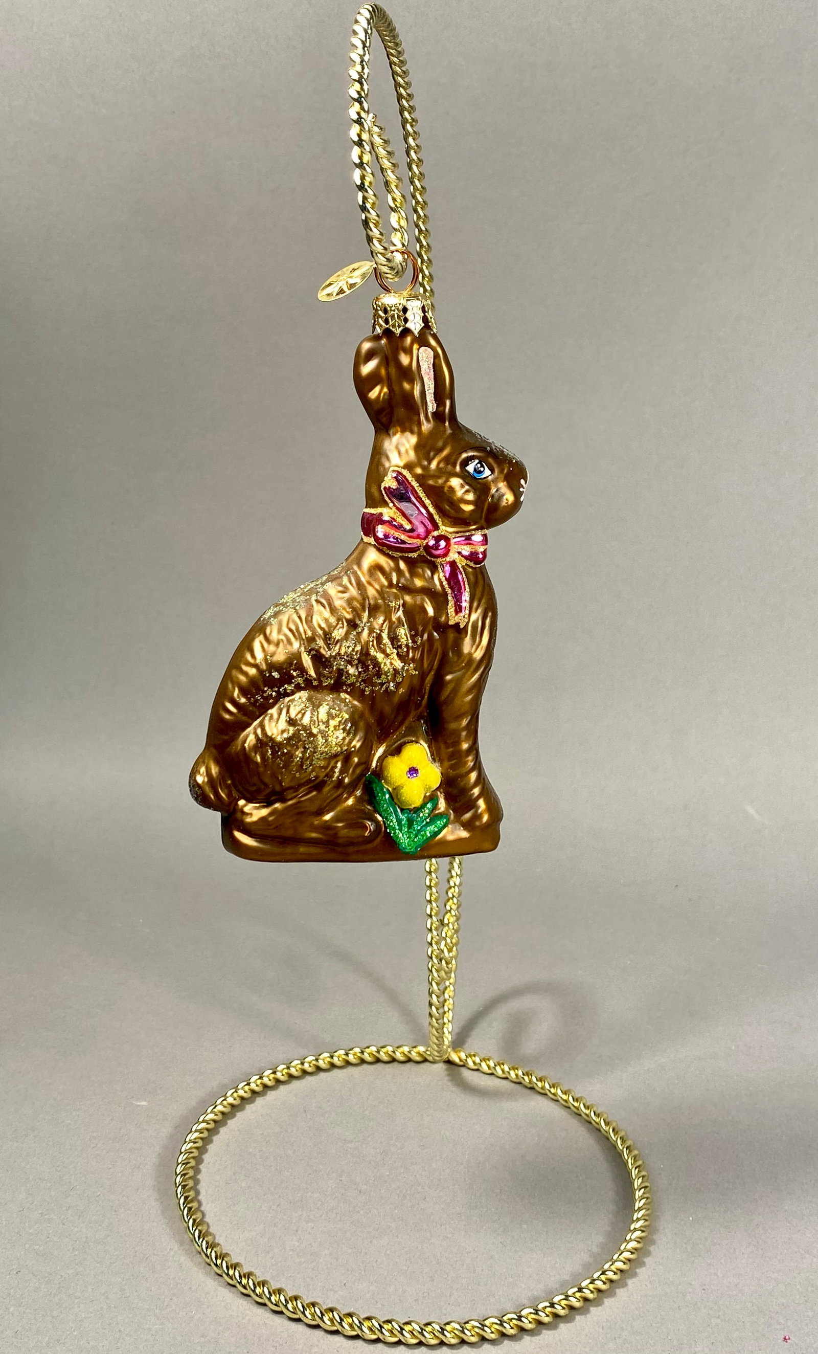 Radko Chocolate Easter Bunny Ornament: This mouth-blown glass holiday ornament is produced by Christopher Radko and depicts a seated chocolate Easter bunny. The piece features a metallic brown finish with hand-painted details including a p