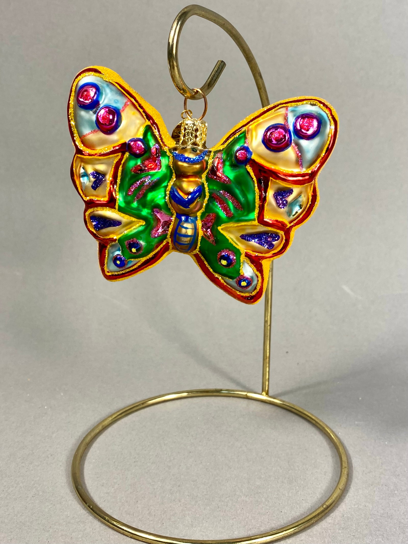 Radko Wings of Gold Blown Glass Butterfly Ornament: **Stand Not Included** A Christopher Radko hand-painted blown glass butterfly ornament from the Wings of Gold collection. This double-sided piece features a central emerald green section accented with