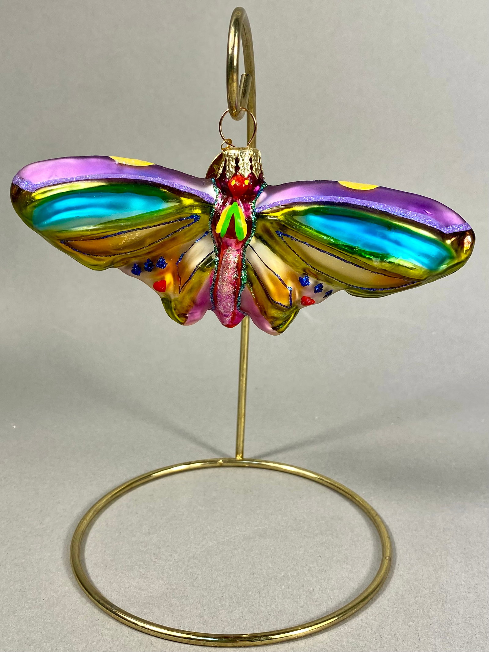 Radko Blown Glass Butterfly Ornament: **Stand Not Included** A hand-blown glass holiday ornament in the form of a butterfly, attributed to Christopher Radko. The piece features a vibrant, multi-colored design with horizontal bands of irid