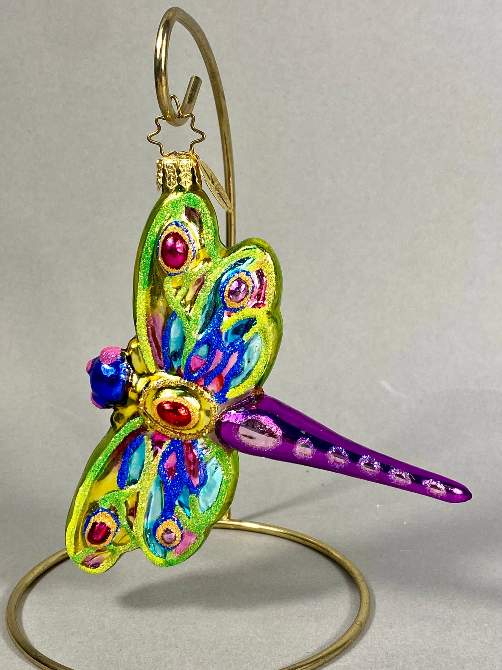 Radko Hand-Blown Glass Dragonfly Ornament: **Stand Not Included** This hand-blown glass ornament by Christopher Radko is designed in the form of a stylized dragonfly. The top of the ornament is fitted with a gold-toned metal cap embossed with 