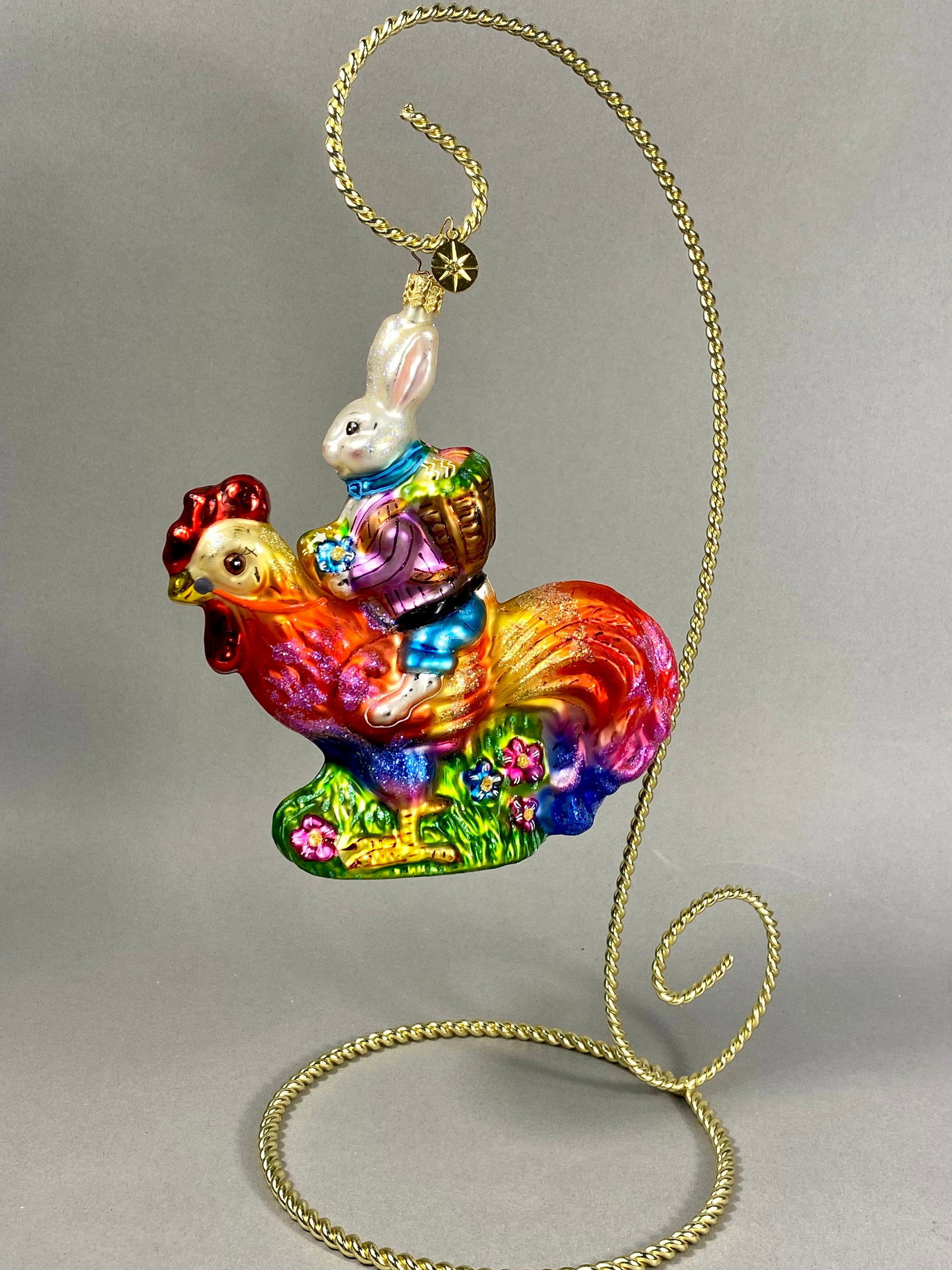 Radko Radiant Rooster Glass Figurine Ornament: **Stand Not Included** This mouth-blown and hand-painted glass holiday ornament is produced by Christopher Radko, identified by the signature eight-pointed star charm attached to the gold-toned hangin