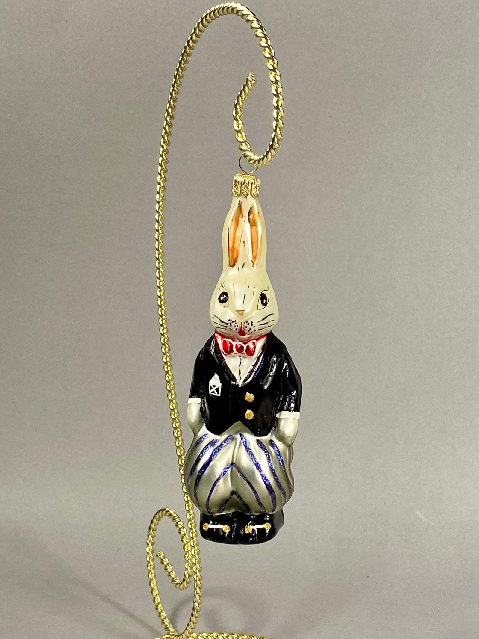 Radko Rabbit in Tuxedo Blown Glass Ornament: **Stand Not Included** Produced by Christopher Radko, this vintage hand-painted blown glass holiday ornament depicts a standing rabbit character in formal attire. The gold-toned fluted metal hanging c
