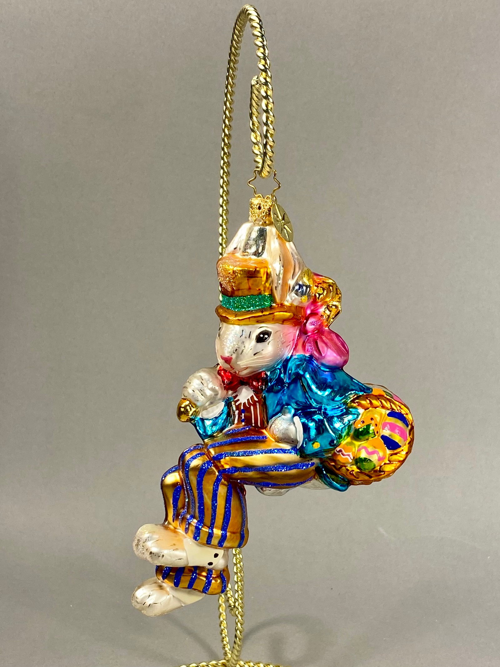Radko Billy Bunny Goes Shopping Glass Ornament: **Stand Not Included** This hand-blown glass holiday ornament is produced by Christopher Radko and titled Billy Bunny Goes Shopping. The ornament is hand-painted with a metallic finish and accented wi