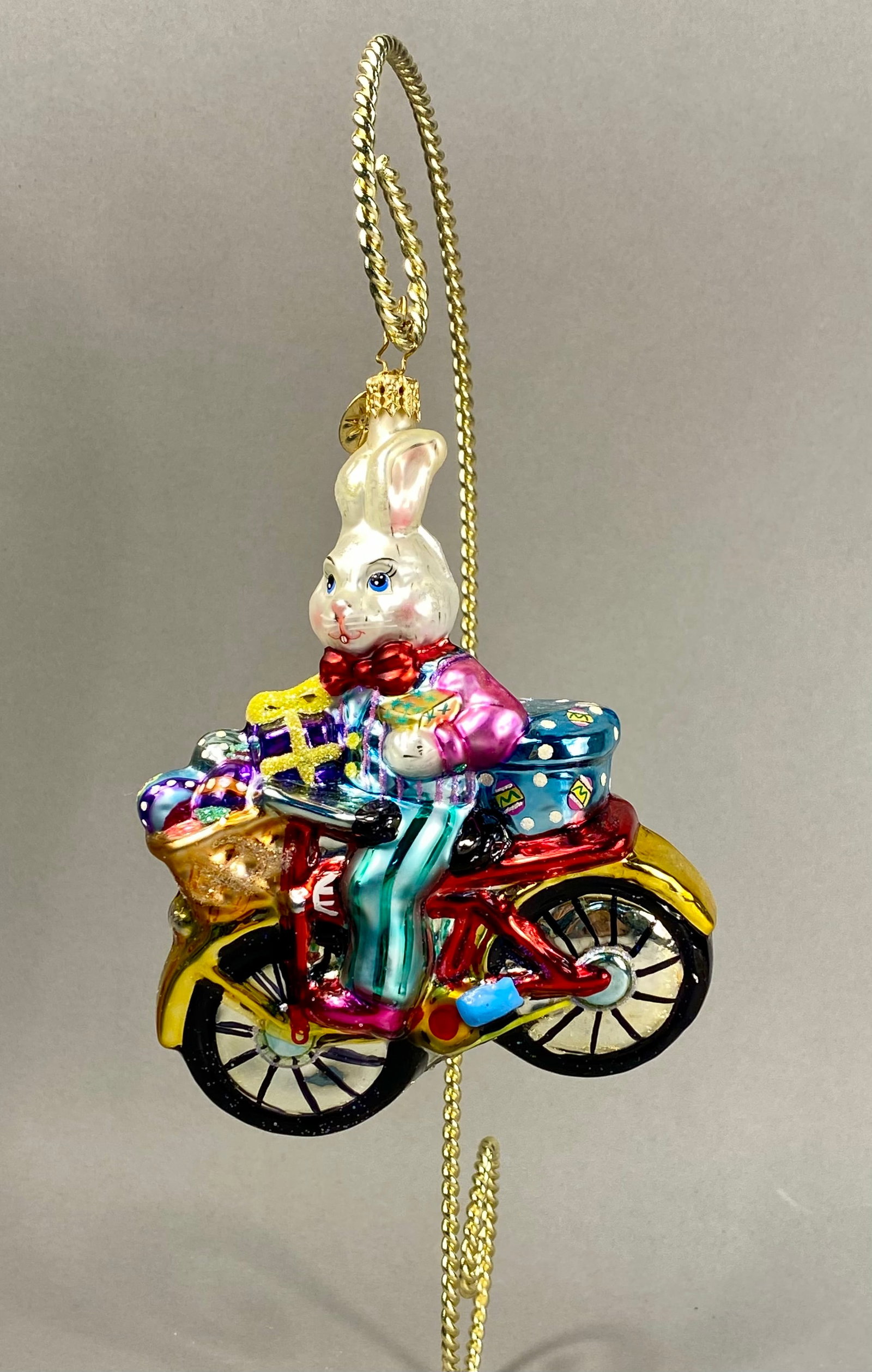 Radko Billy Bunny Goes Shopping Hand Blown Glass Ornament: **Stand Not Included** A hand-blown glass holiday ornament titled Billy Bunny Goes Shopping by Christopher Radko. The ornament depicts a white rabbit character dressed in a pink jacket, red bow tie, a