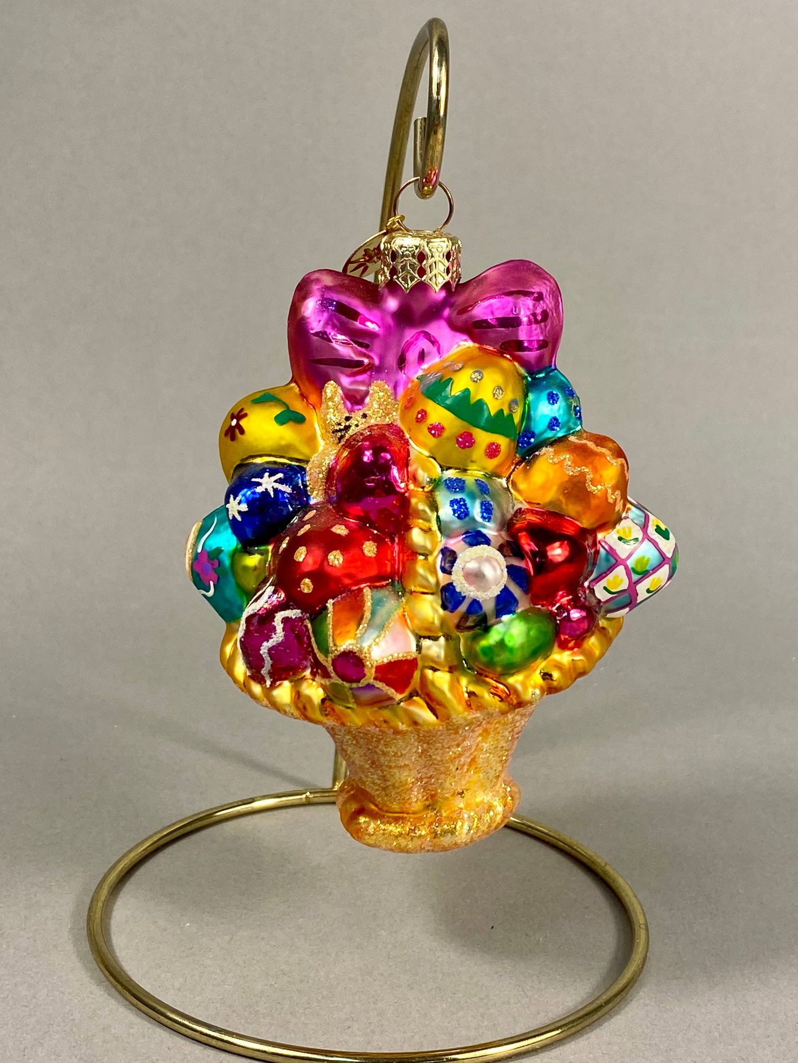 Christopher Radko Hand-Painted Blown Glass Easter Basket Holiday Ornament: A hand-crafted blown glass holiday ornament by Christopher Radko, designed in the form of an ornate Easter basket. The basket is overflowing with detailed elements including multiple decorated eggs fe