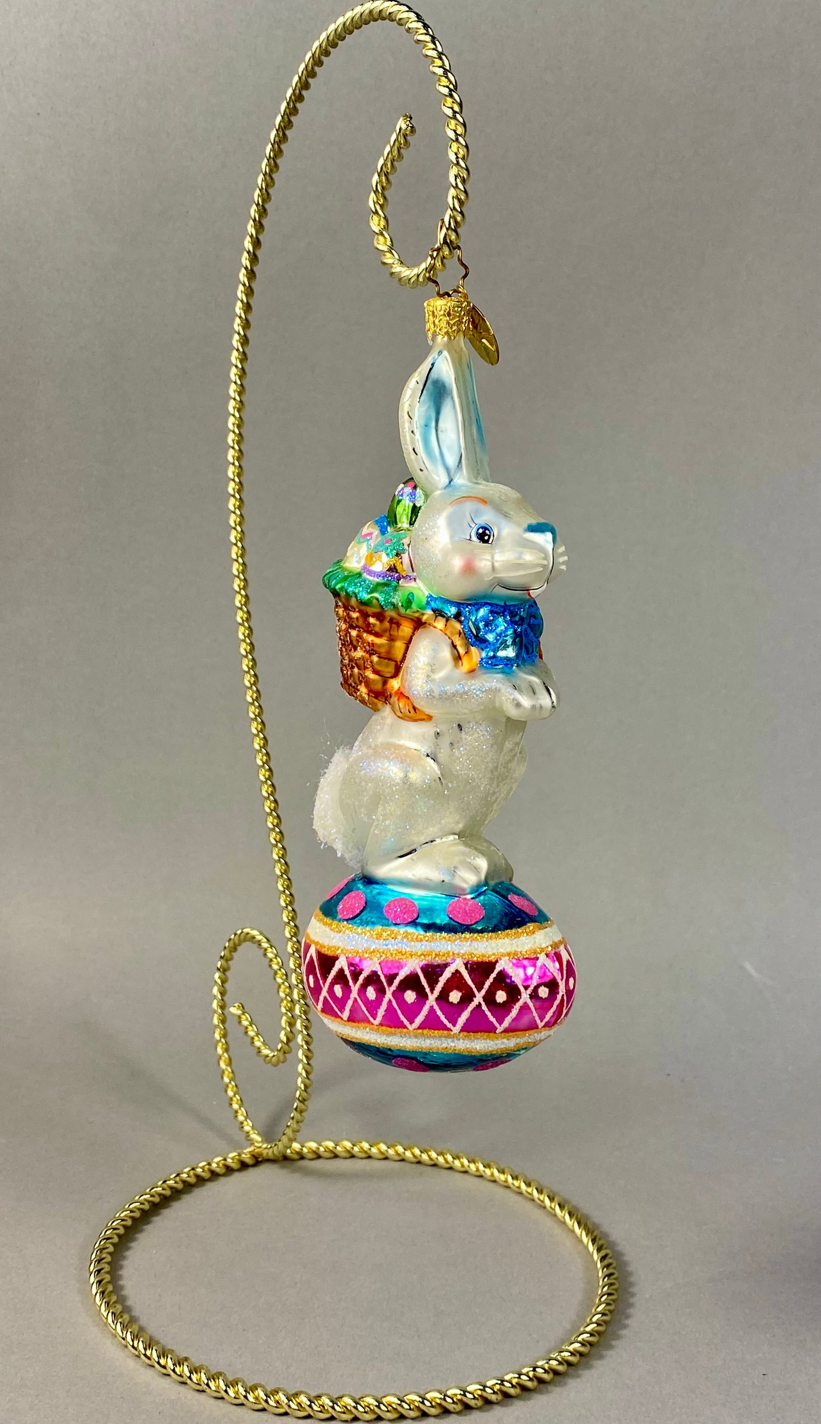Christopher Radko Hoppy Holidays Glass Easter Bunny Ornament: This hand-blown glass holiday ornament is a Christopher Radko creation in the Hoppy Holidays pattern. It features a standing white iridescent bunny rabbit wearing a blue glittered bow around its neck.