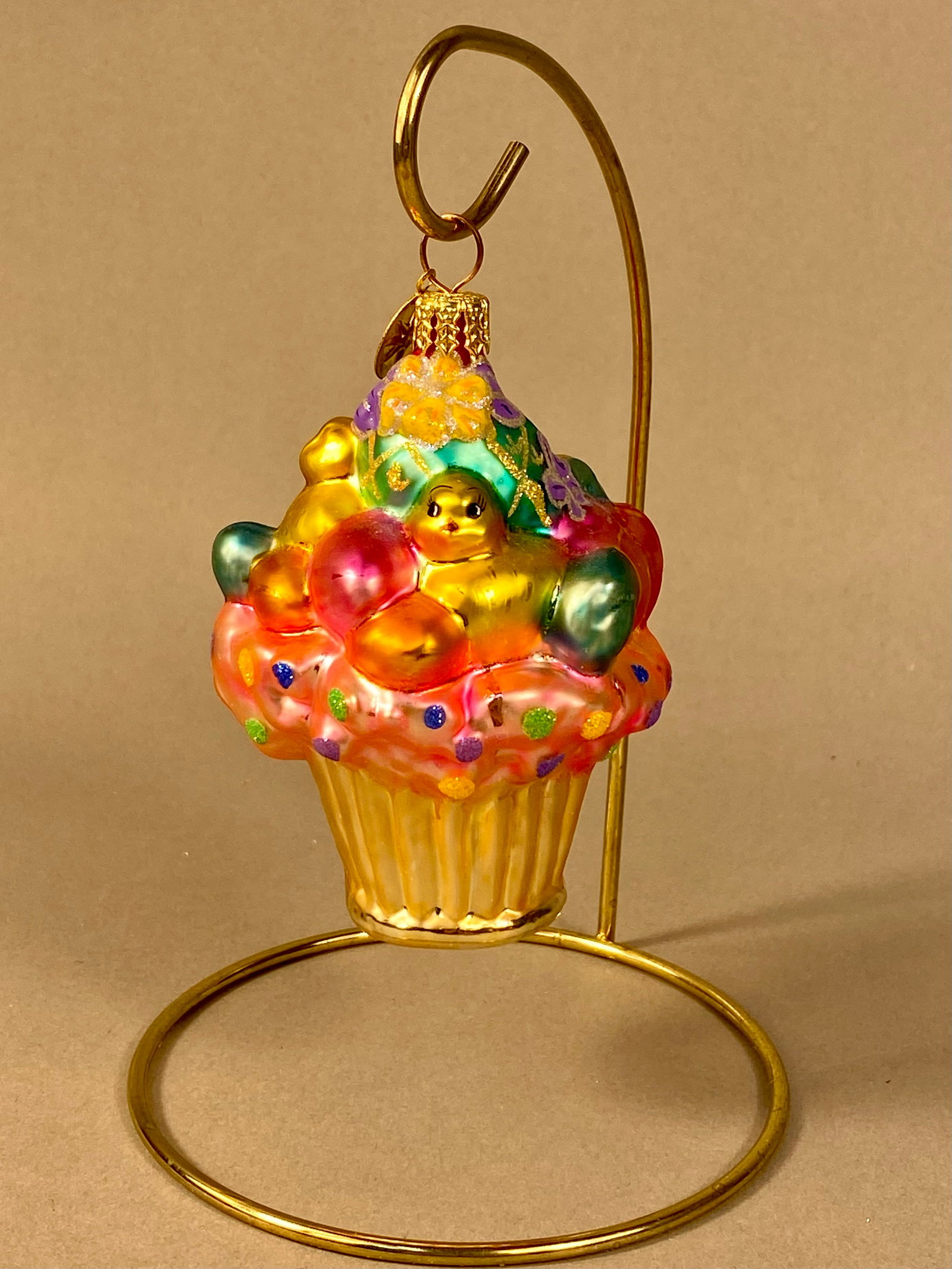 Christopher Radko Hand-Painted Glass Easter Cupcake Ornament: This is a mold-blown glass ornament from Christopher Radko, featuring an elaborate Easter-themed cupcake design. The base is shaped like a gold-toned ribbed cupcake liner. The frosting is composed of 