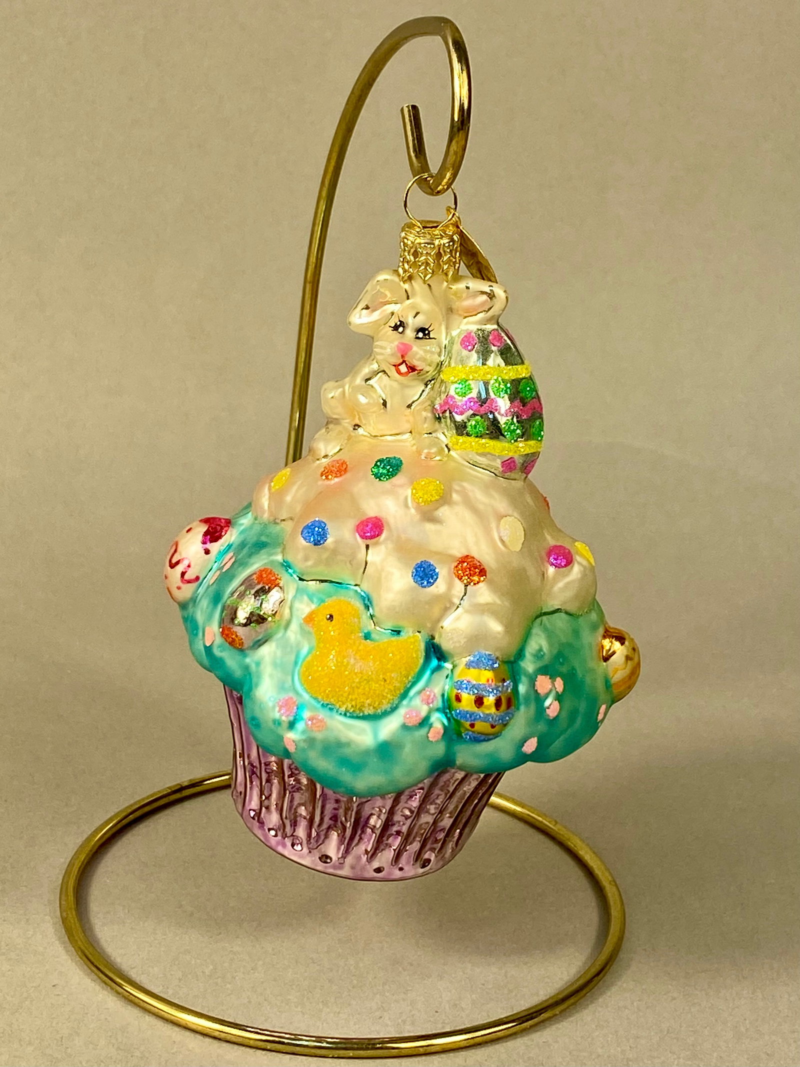 Christopher Radko Bakery Tweets Easter Bunny Cupcake Glass Ornament: This hand-blown glass ornament was produced by Christopher Radko and is part of the Bakery Tweets collection. The piece is modeled as a multi-layered Easter cupcake. A white rabbit sits at the top, ho