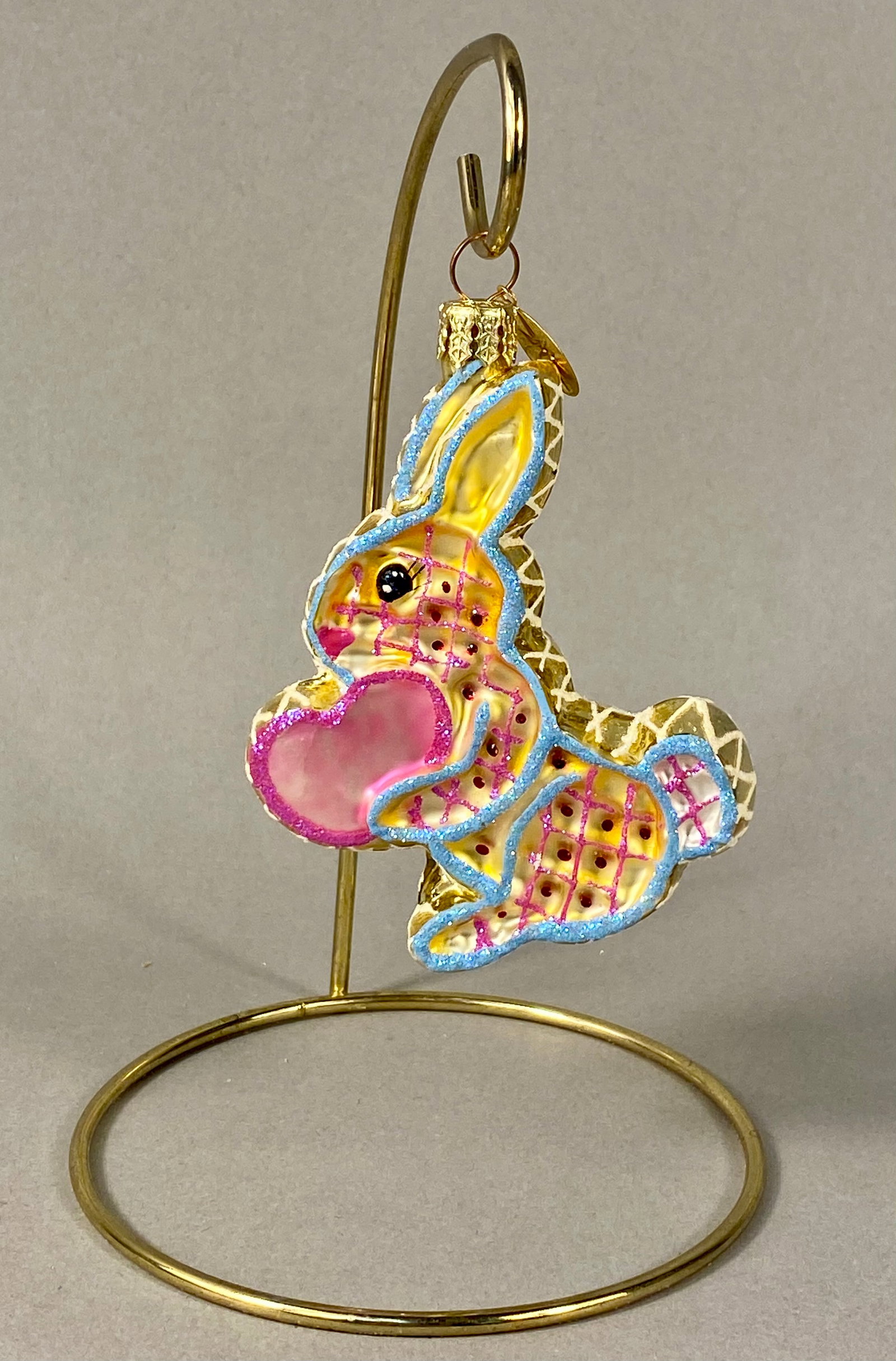 Christopher Radko Hoppy Holidays Glass Bunny Rabbit Ornament: This is a mouth-blown glass holiday ornament by Christopher Radko, identified as the Hoppy Holidays pattern. The ornament depicts a stylized yellow rabbit in a seated position holding a large, translu