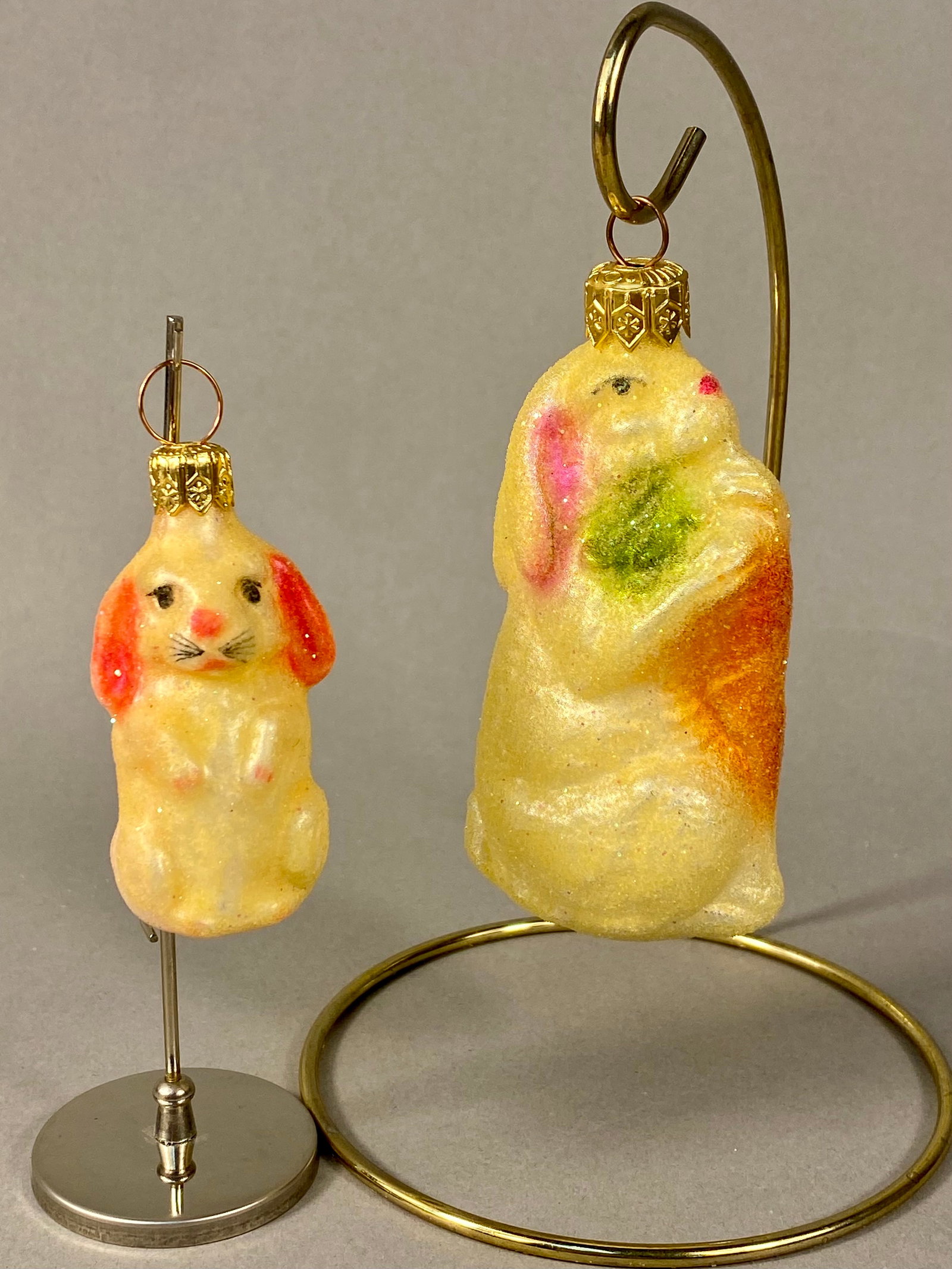 A Pair of Christopher Radko Blown Glass Rabbit Holiday Ornaments: This pair of hand-painted blown glass holiday ornaments is produced by Christopher Radko. The set consists of two distinct rabbit figurines. One ornament features a small, front-facing rabbit with pin