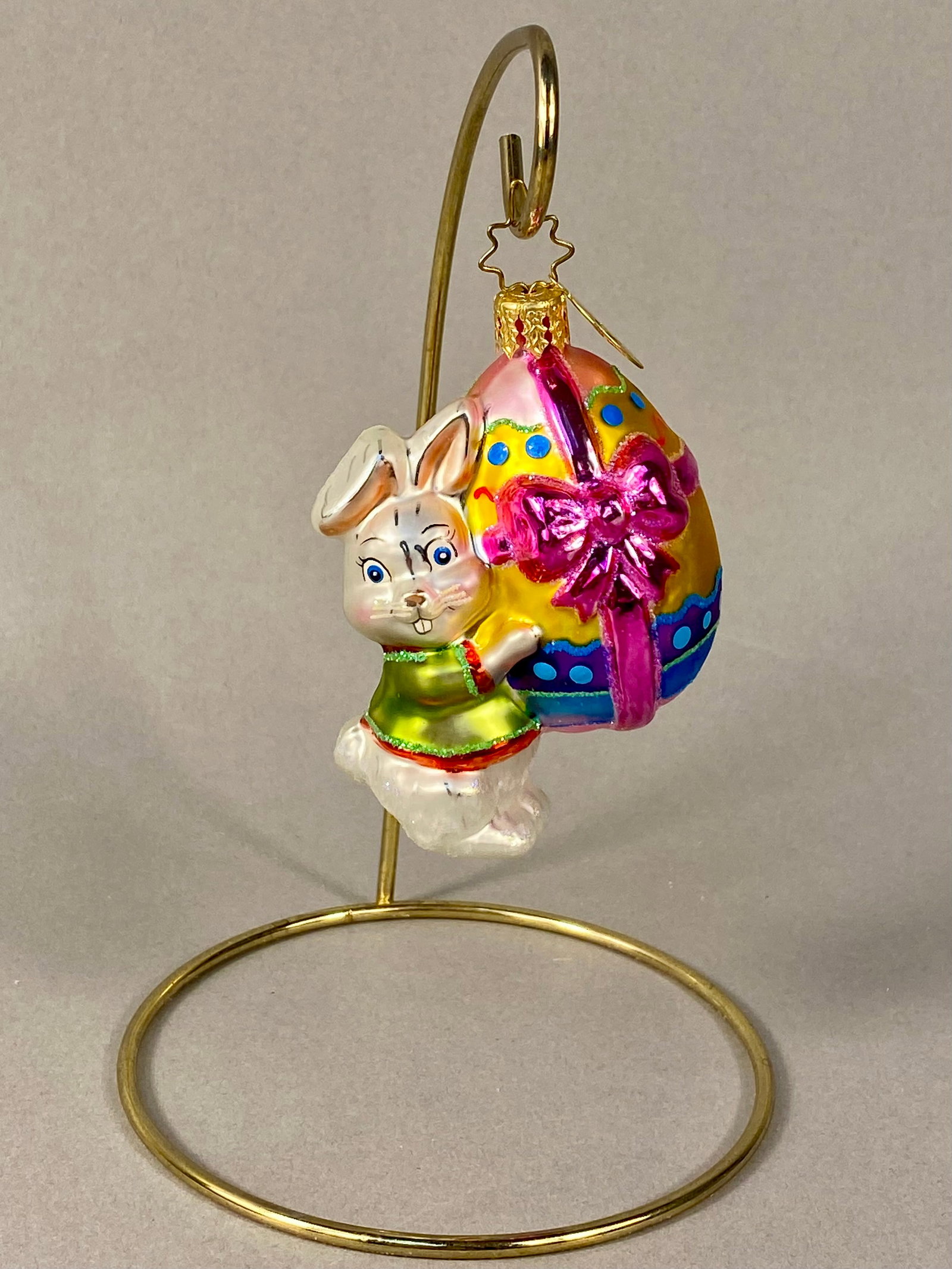 Christopher Radko Hoppy Holidays Easter Bunny and Egg Glass Ornament: Christopher Radko mouth-blown glass holiday ornament titled Hoppy Holidays. The ornament depicts an anthropomorphic white rabbit with blue eyes and pink inner ears, shown clutching a large, vibrantly 