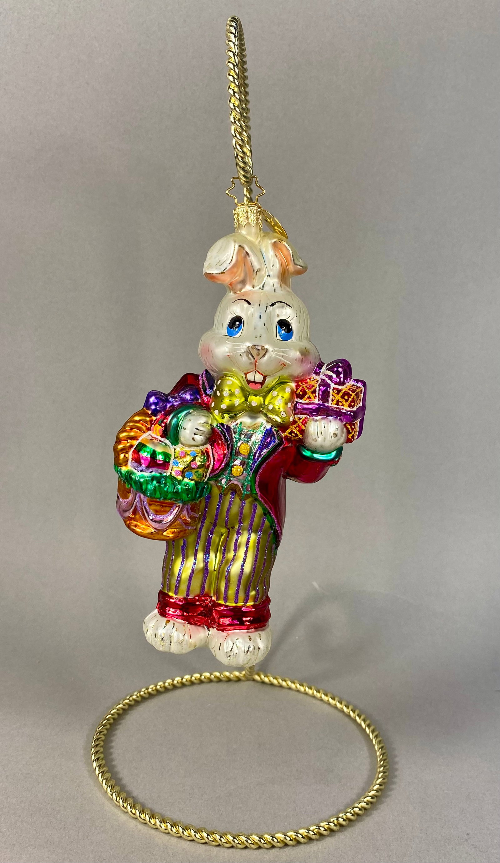 Christopher Radko Billy Bunny Goes Shopping Glass Easter Ornament: This hand-blown glass ornament is a Christopher Radko design titled Billy Bunny Goes Shopping. The figurine depicts an anthropomorphic rabbit dressed in festive attire, including a metallic red frock 