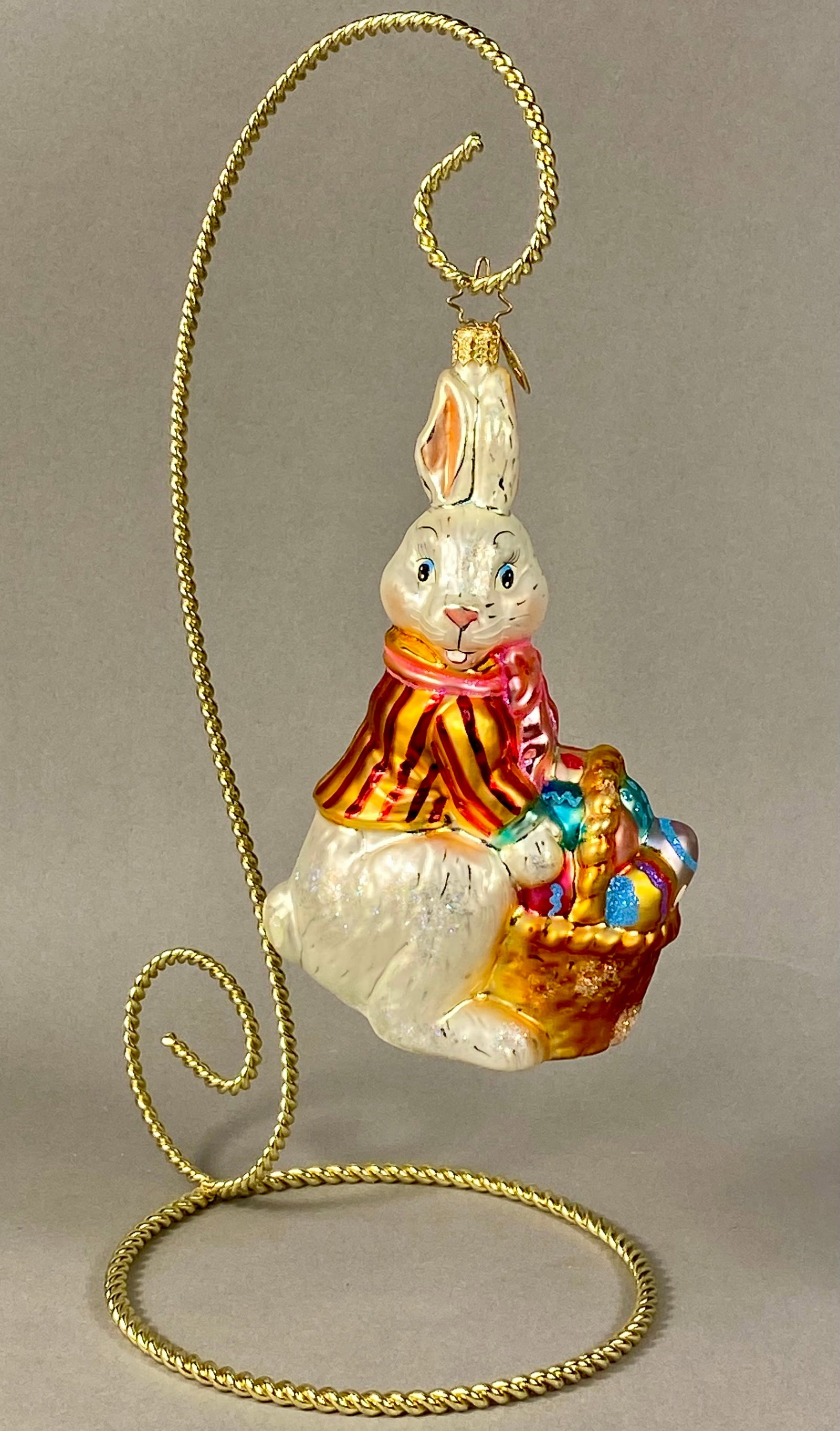 Christopher Radko Mouth-Blown Glass Hoppy Holidays Easter Bunny Ornament: This is a mouth-blown glass holiday ornament by Christopher Radko, identified as the Hoppy Holidays pattern. The figure depicts an anthropomorphic bunny in a seated pose, wearing a yellow and reddish-