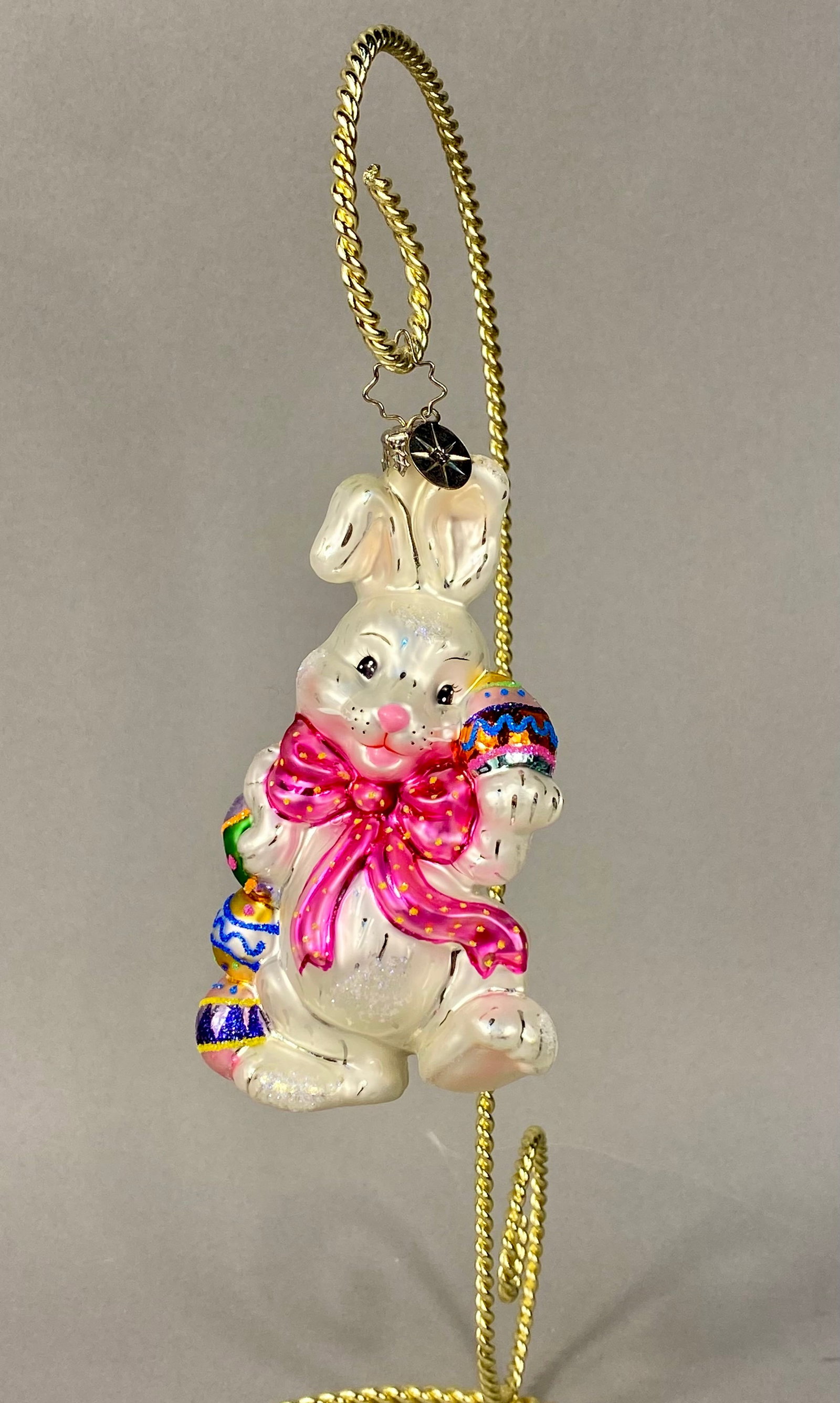 Christopher Radko Hoppy Holidays Easter Bunny Glass Ornament: A Christopher Radko hand-blown glass holiday ornament identified as the Hoppy Holidays pattern. The ornament depicts a standing rabbit in a pearlescent white finish with hand-painted features. The fig